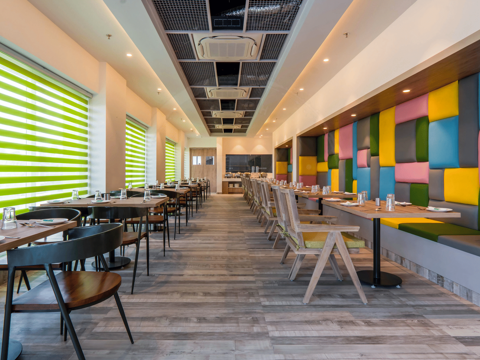 Full view of the dining area featuring a wooden floor along with colourful cushioned panels mounted on the wall at Hotel Le Roi, Dehradun.