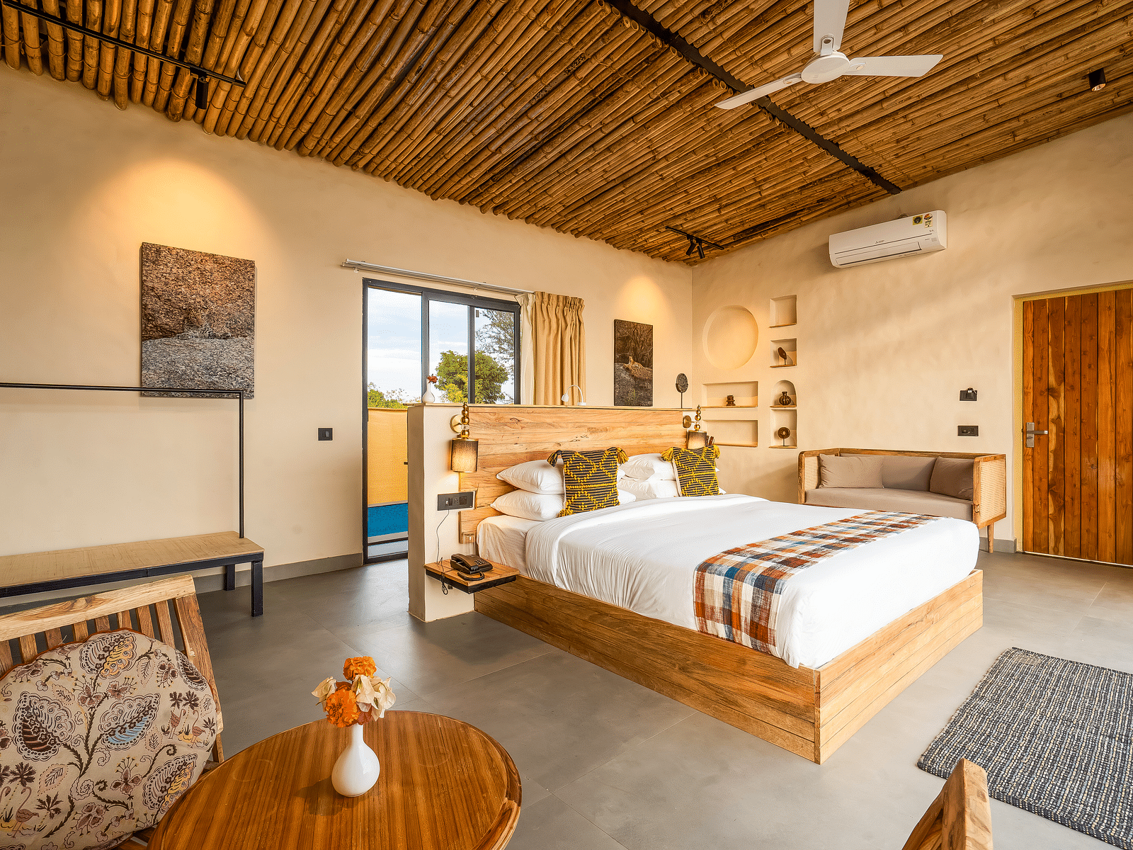 An image of a wooden furnished bedroom  featuring a double size bed, a  chair and centre table, a sofa, AC, fan,  and some decorative items - Kurja Jawai