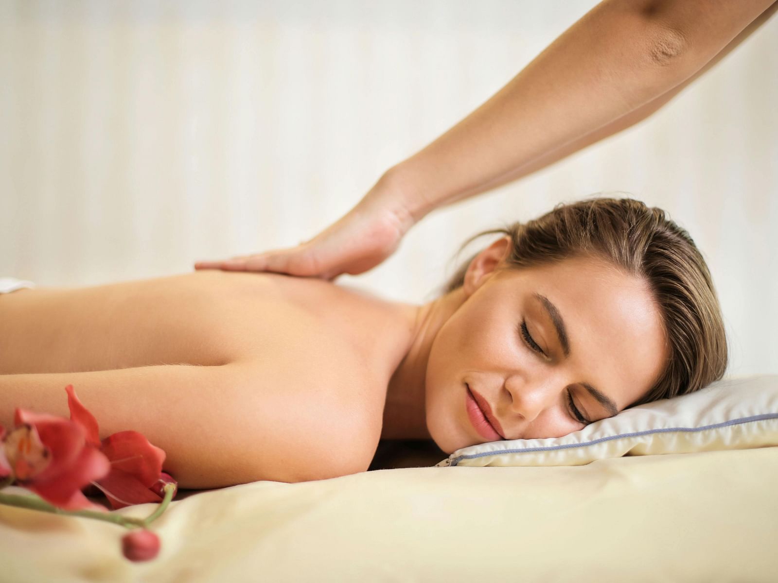 A lady getting a treatment done at a spa with flowers kept on side.