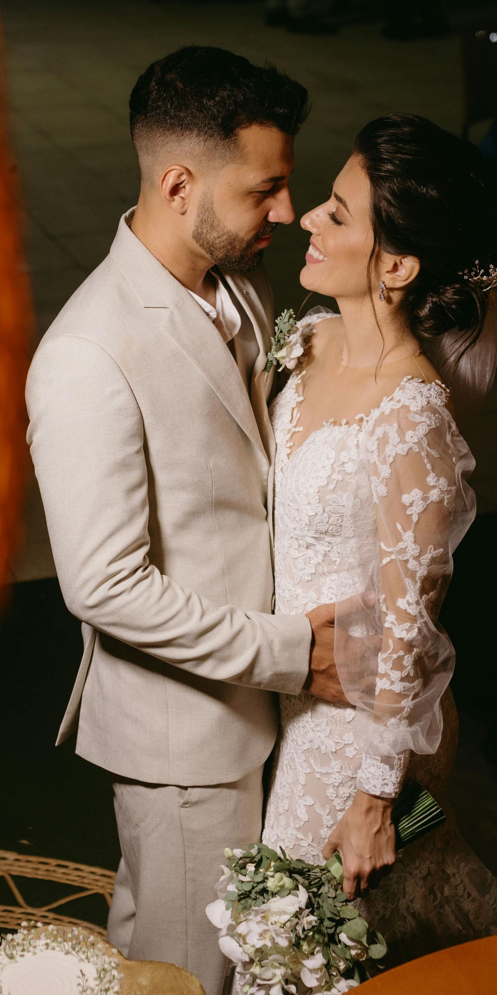 a couple close to each other dressed in western wedding attire with a blurry bamboo lamp in front of them
