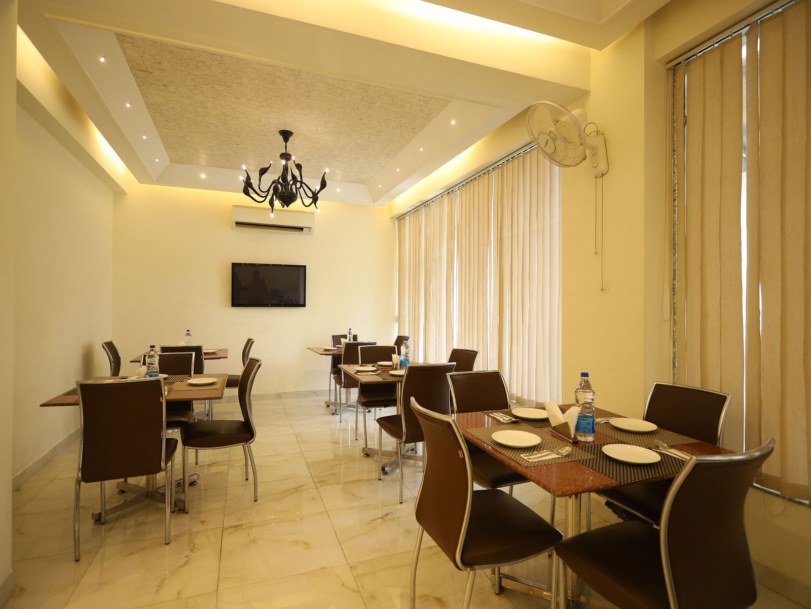 A well-lit dining space with several tables and chairs is decorated with sheer curtains and a chandelier - Asian Suites Cyber Park, Gurgaon