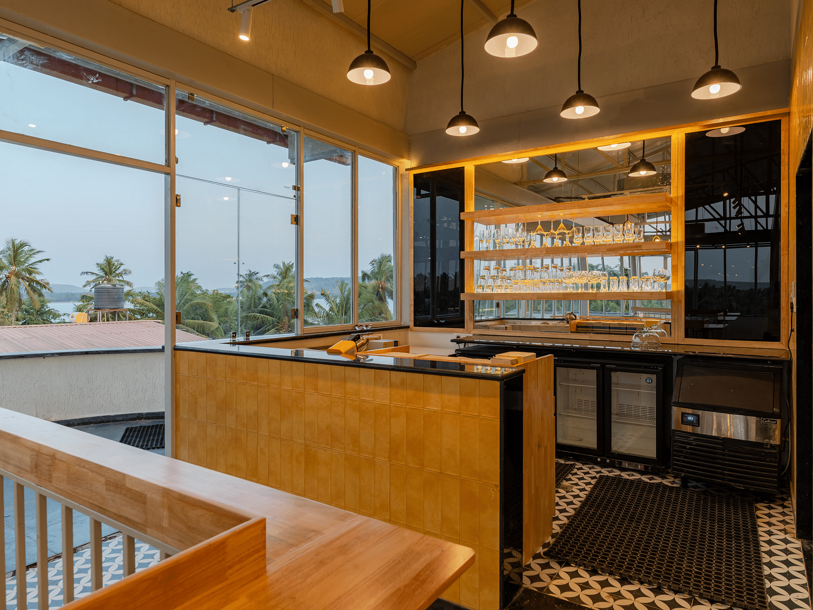 An elegant bar area with a wooden counter and backlit shelves, creating a sophisticated space for guests to enjoy a selection of fine wines and spirits in a modern, yet cosy ambiance  at Bedzzz Xclusiv Morjim, Goa