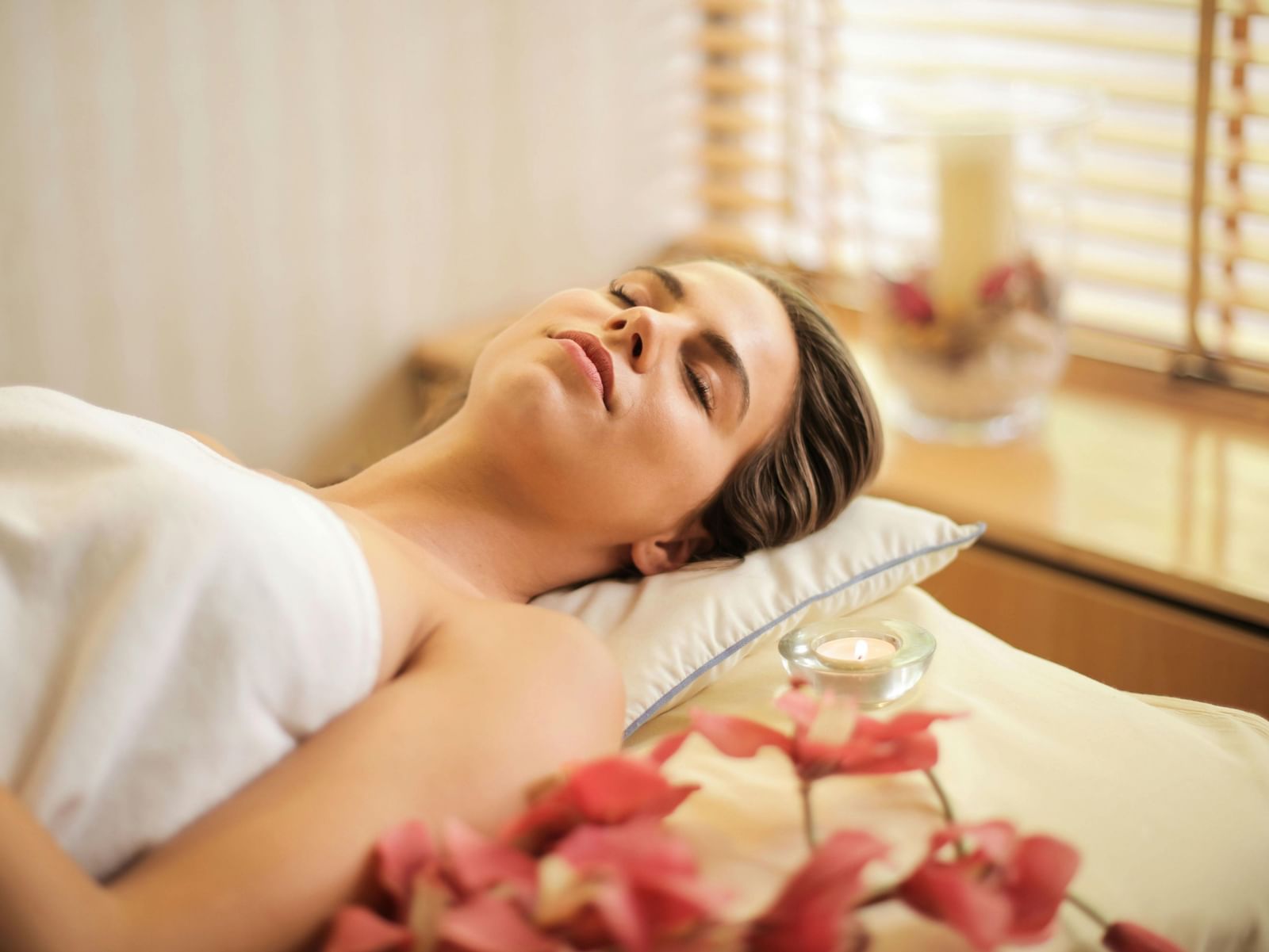 A person lying down with their eyes closed and a peaceful expression while receiving a spa treatment.