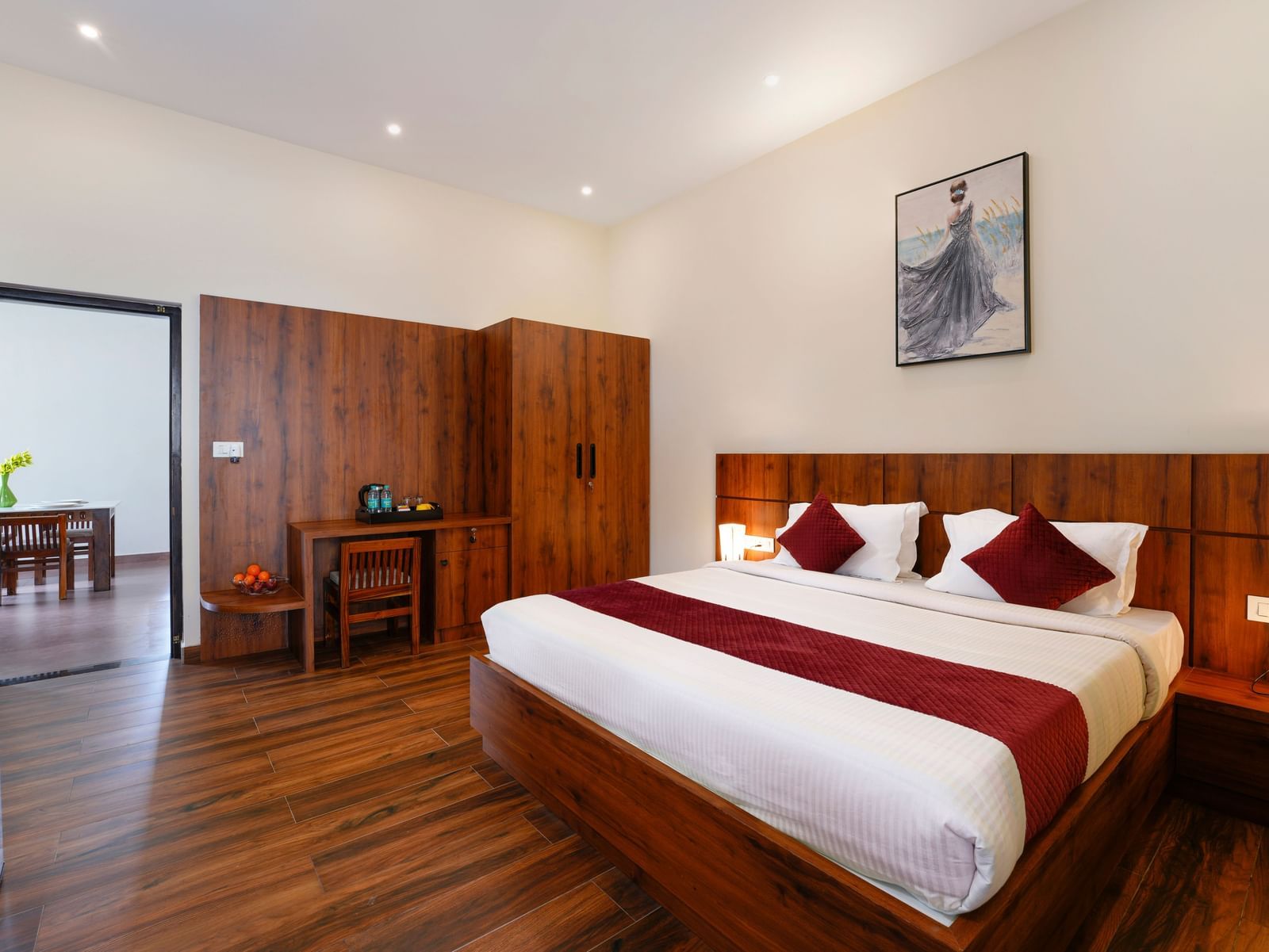 A comfortable bedroom in the villa at Bhuthanakadu Retreat, featuring a large wooden bed with a maroon and white duvet, and dark wooden furniture.