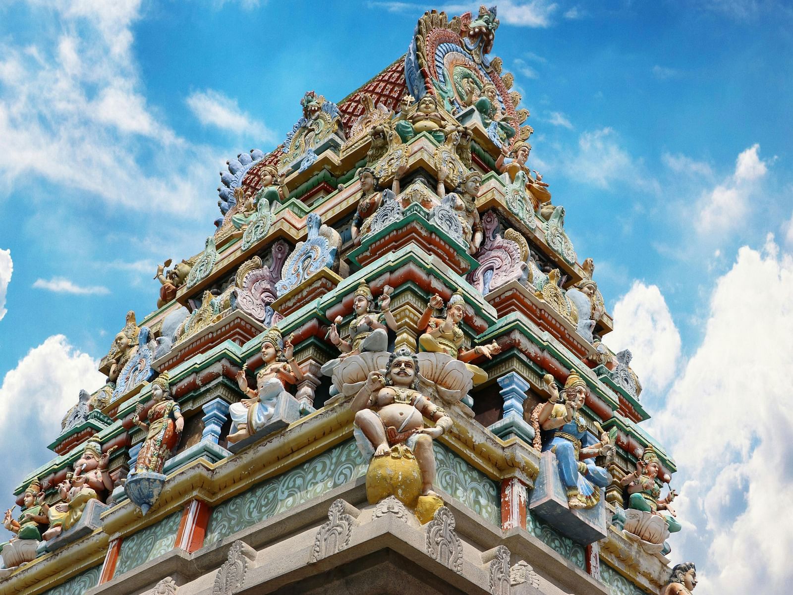 A wide view of the temple featuring intricate stone carvings on the top, showcasing detailed architectural design with moving clouds in the background.