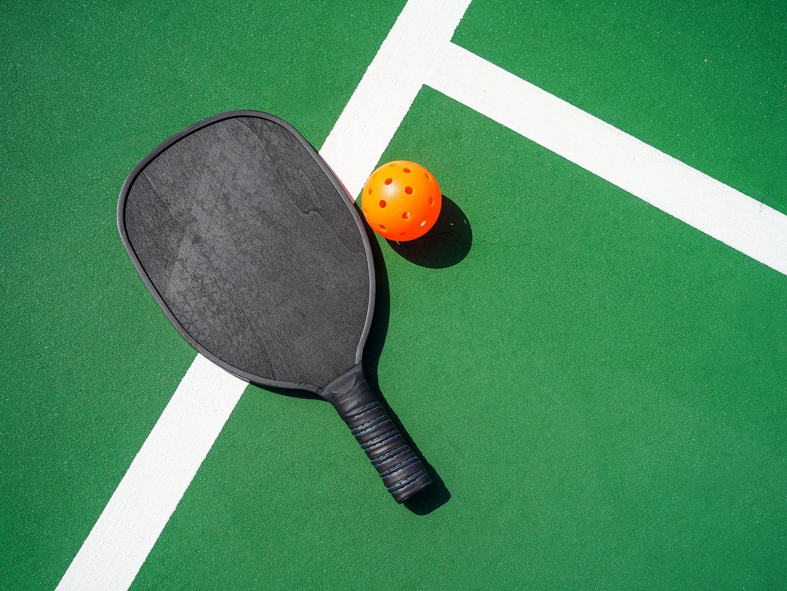 Image of a pickle ball and its racket kept on a green coloured court