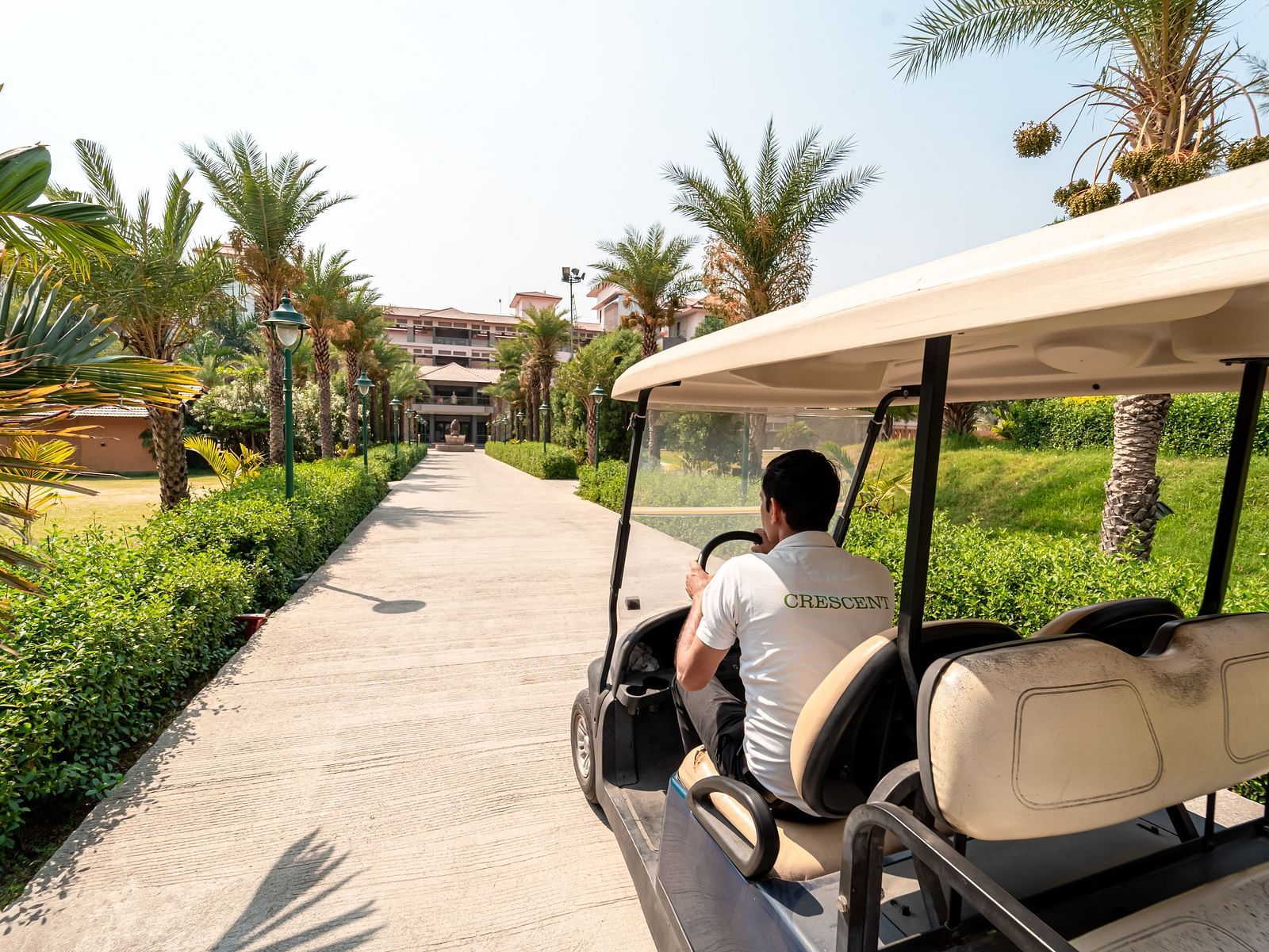 A person driving a golf cart along the footpath at Crescent Spa & Resort, Indore, surrounded by scenic resort views