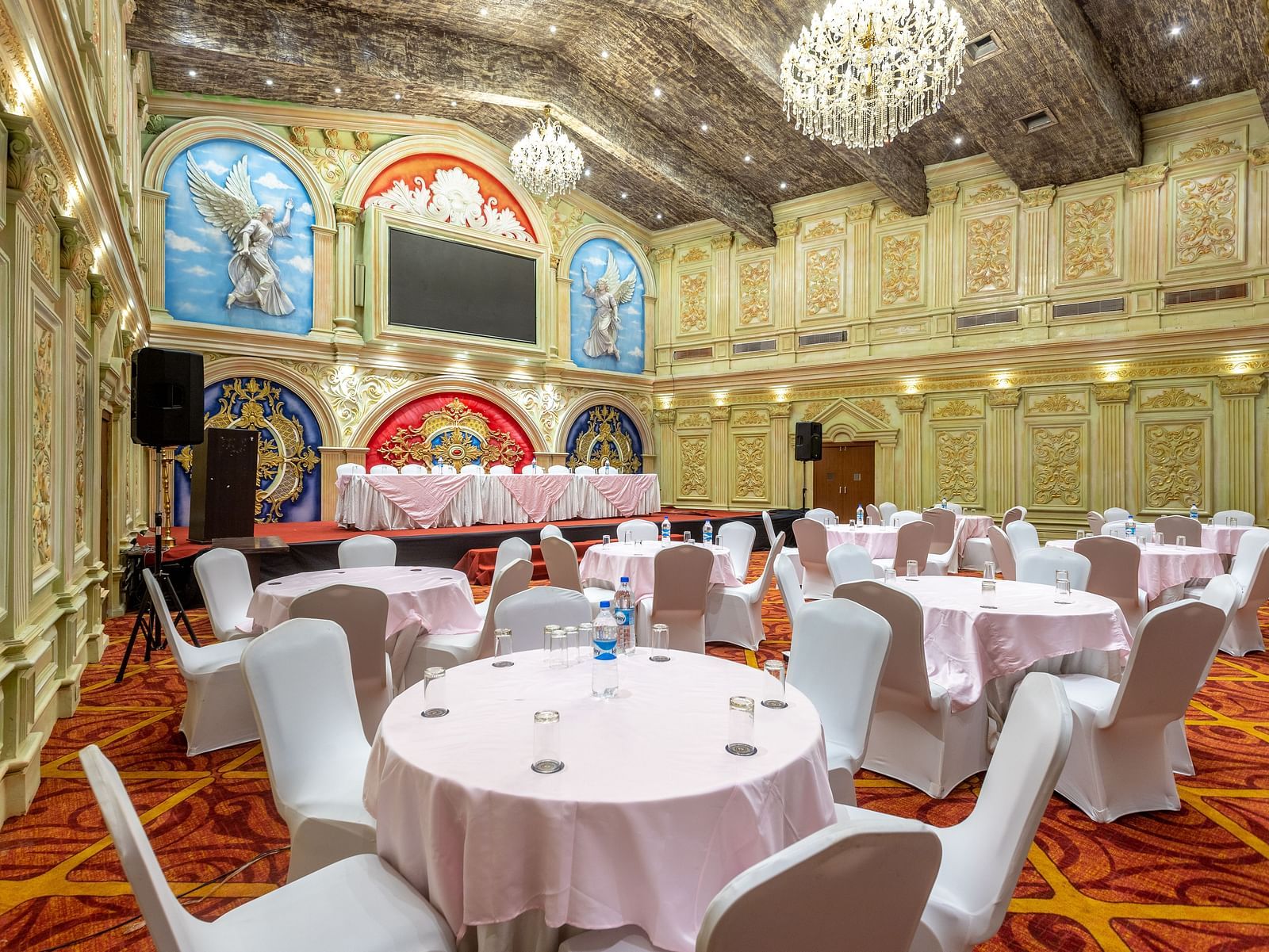 Ornate banquet hall at Diamond Palace Lords Plaza with round tables, chairs, chandeliers, and decorative walls.