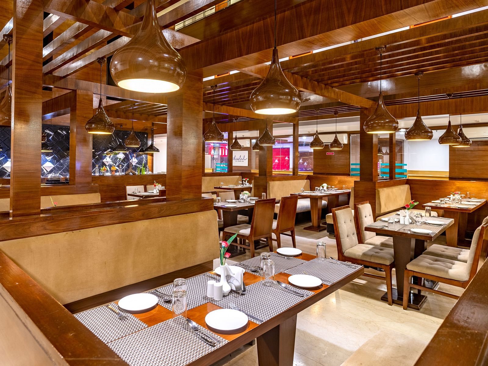 Warmly lit restaurant at Diamond Palace Lords Plaza with wooden beams, set tables, and booth seating.