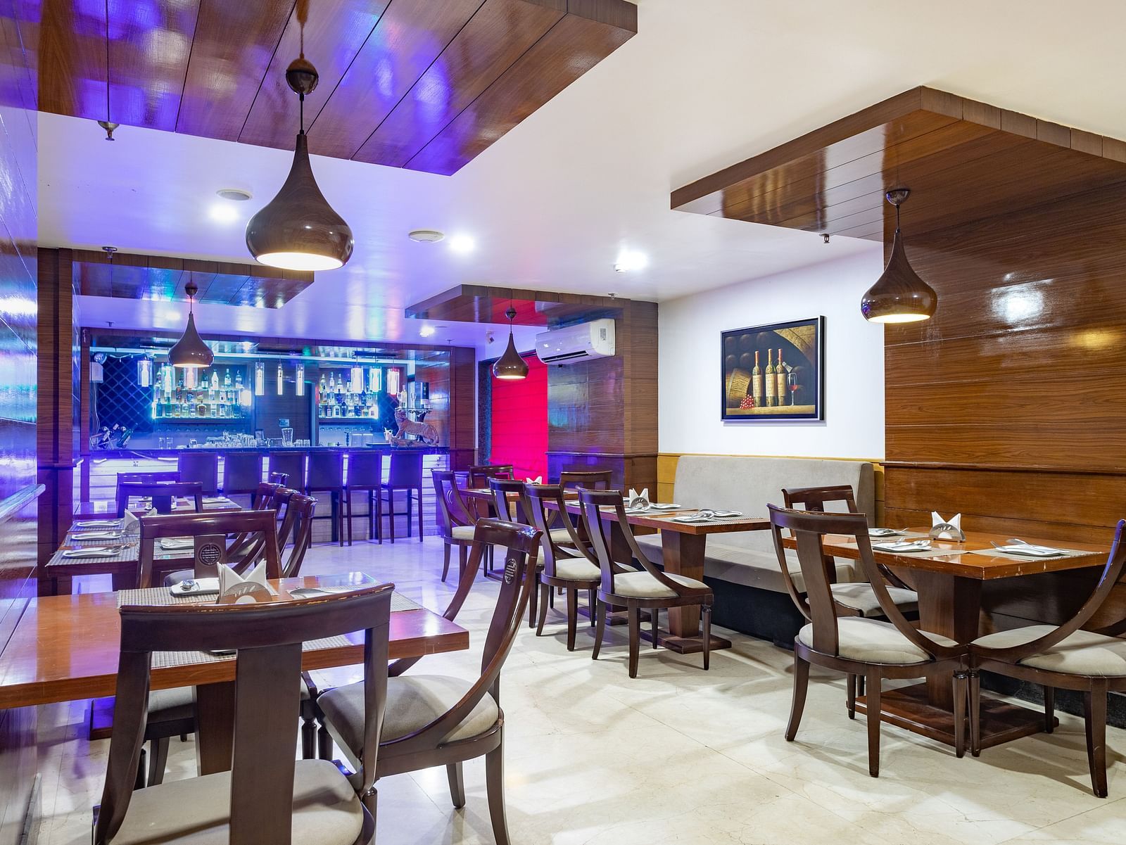 Modern restaurant at Diamond Palace Lords Plaza with wooden tables, chairs, pendant lights, and a bar area.