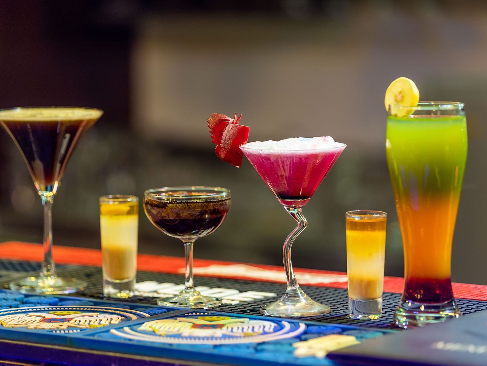 Assortment of colorful cocktails and shot glasses arranged on a bar counter with a blurred background.