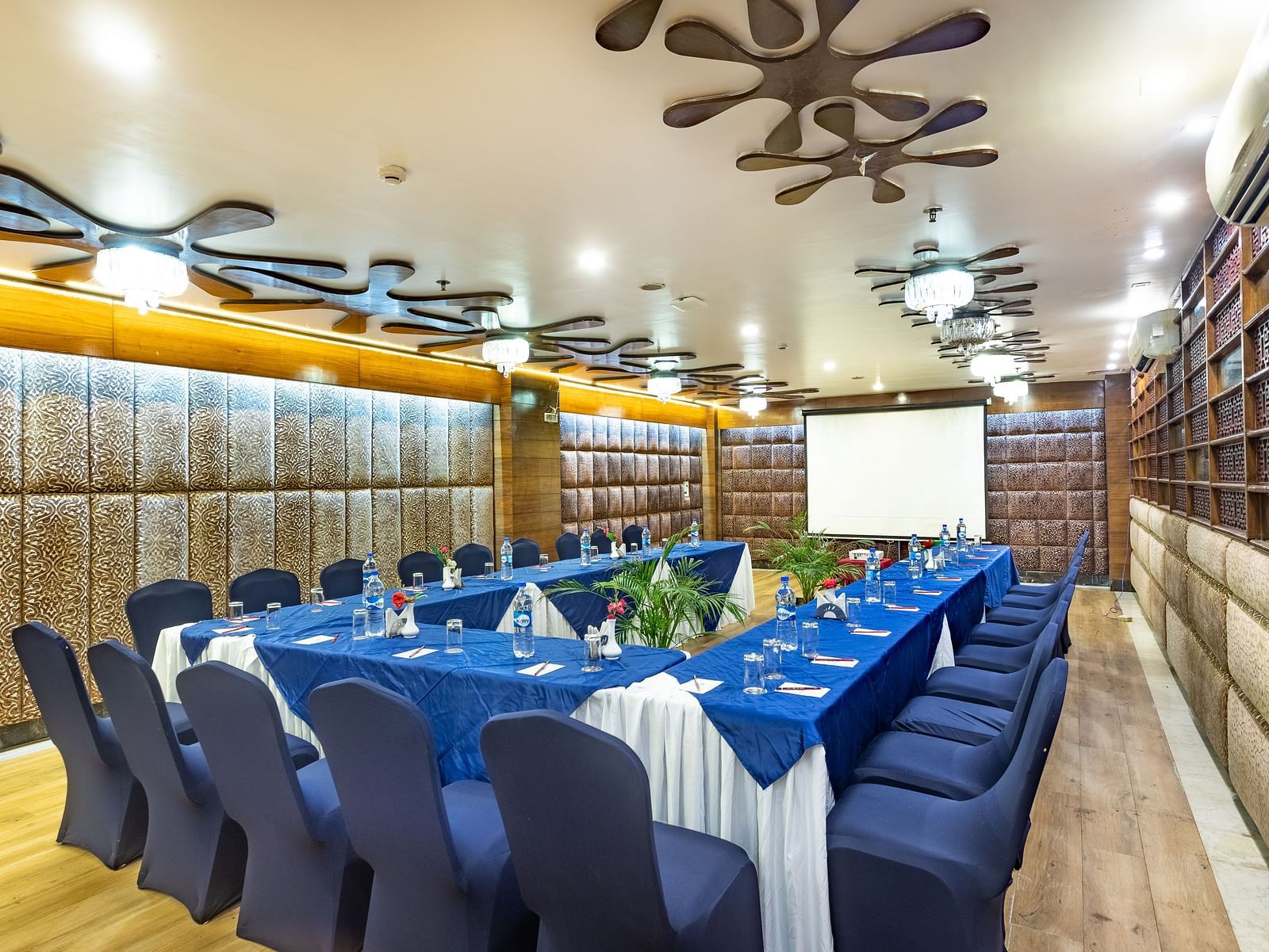 Meeting room with a U-shaped table covered in fabric, facing a projection screen and decorated walls.