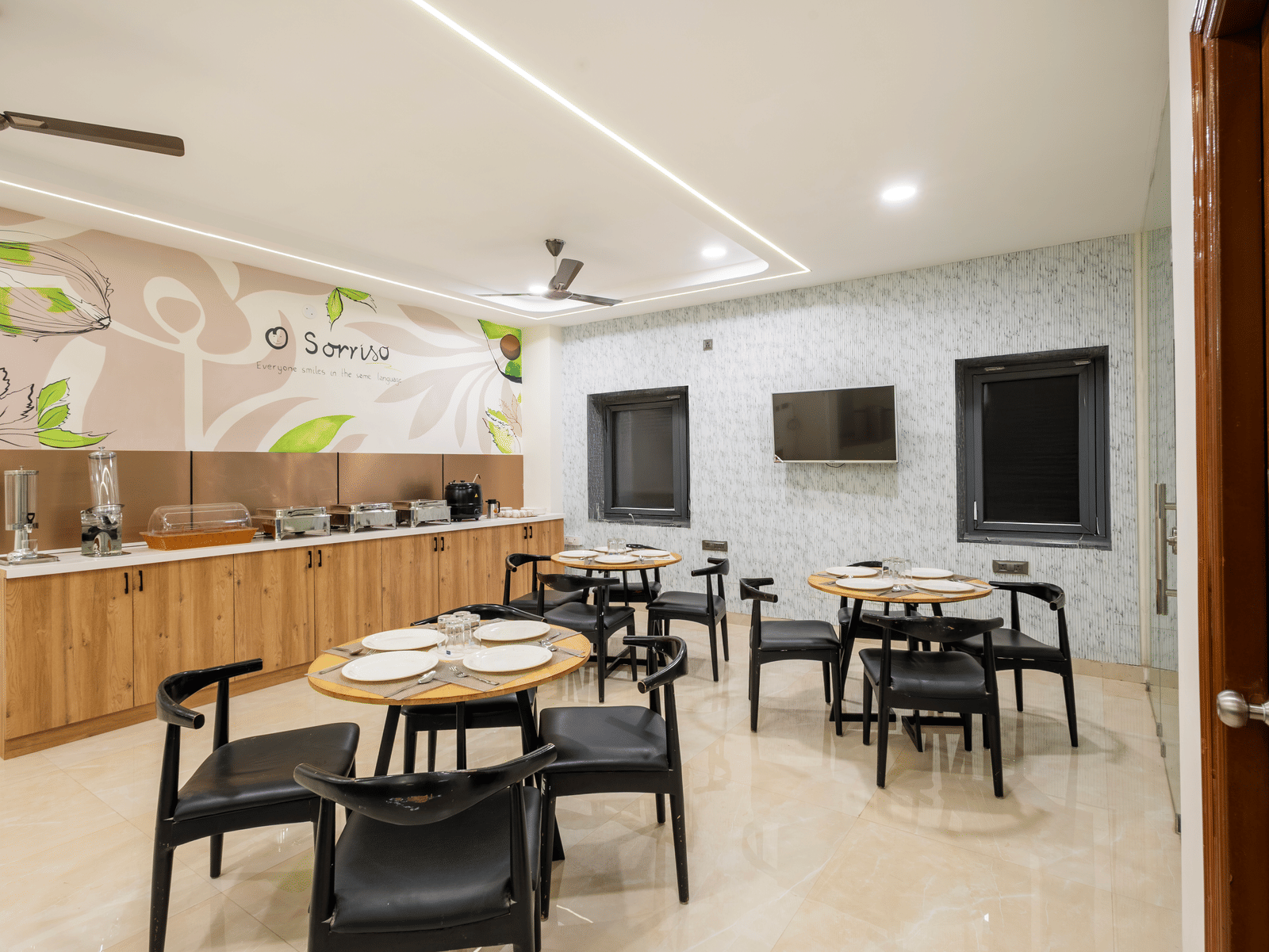 A dining area with tables and chairs at Elysium Studio Suites, Madhapur, has wall decorations and overhead lights.