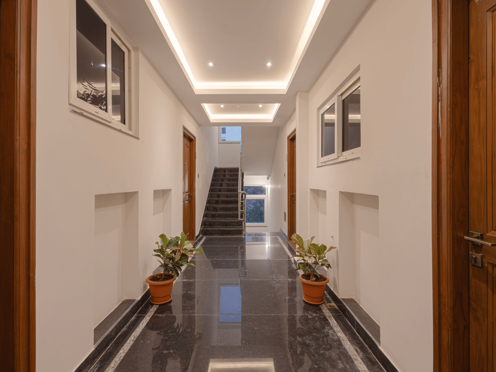 A long hallway at Elysium Studio Suites, Madhapur, with walls, potted plants, and multiple doors leading off it.