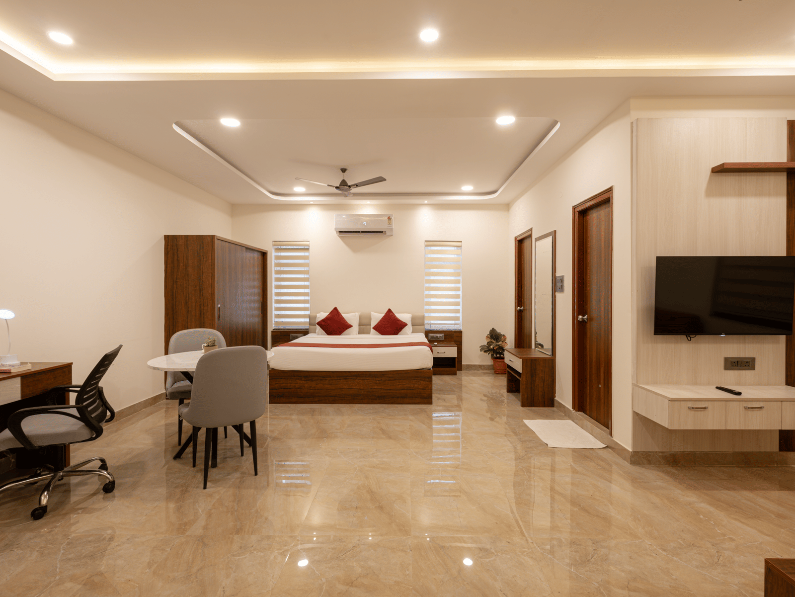 A panoramic view of a room at Elysium Studio Suites, Madhapur, shows a bed, desk, and chair on the left and right.