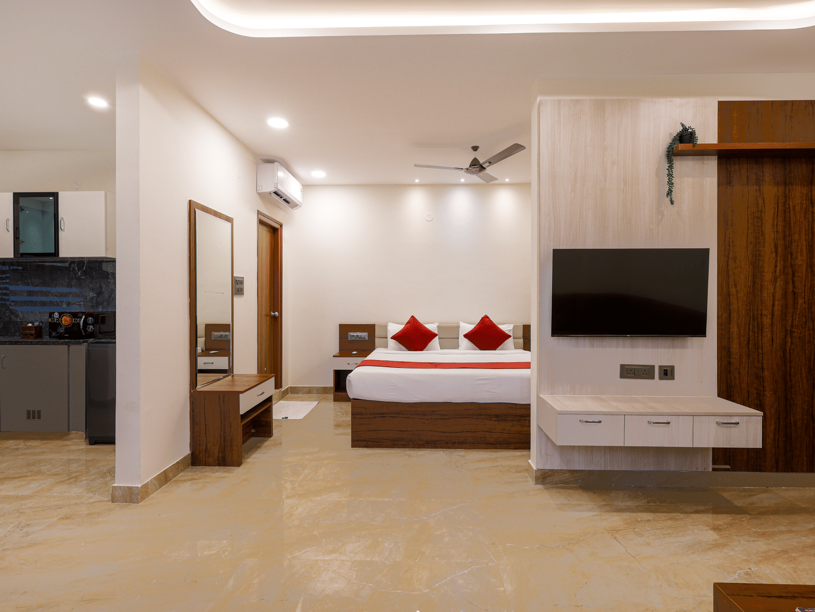 A room at Elysium Studio Suites, Madhapur, shows a bed, a desk, and a television mounted above a storage unit.