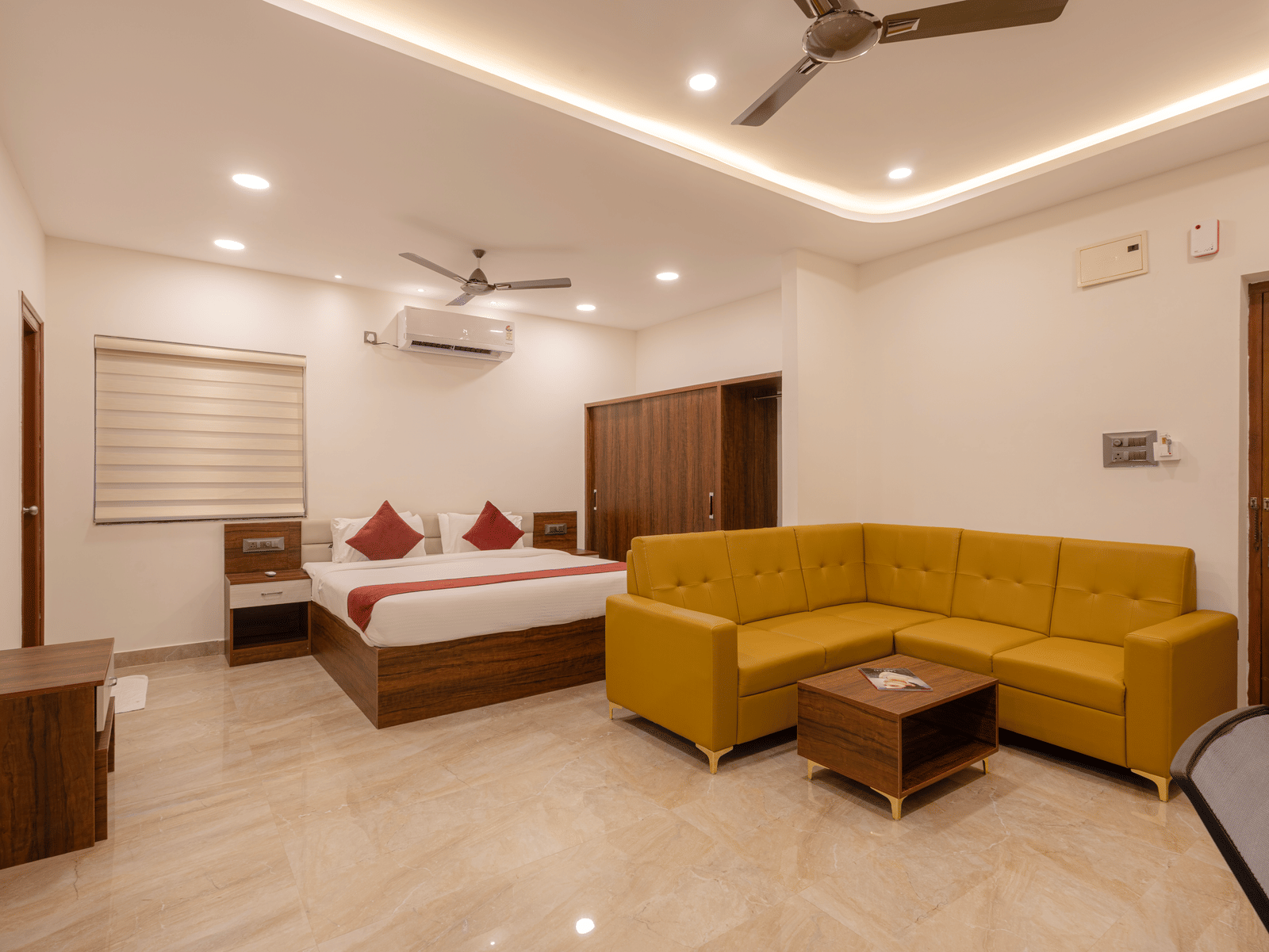 A room at Elysium Studio Suites, Madhapur, shows a bed, a yellow sofa, and a table on a tiled floor.
