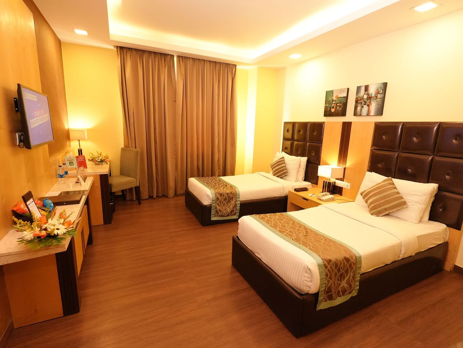Hotel room with a bed featuring striped bedding and a television on the wall - Grand Plaza Lords Inn Jammu