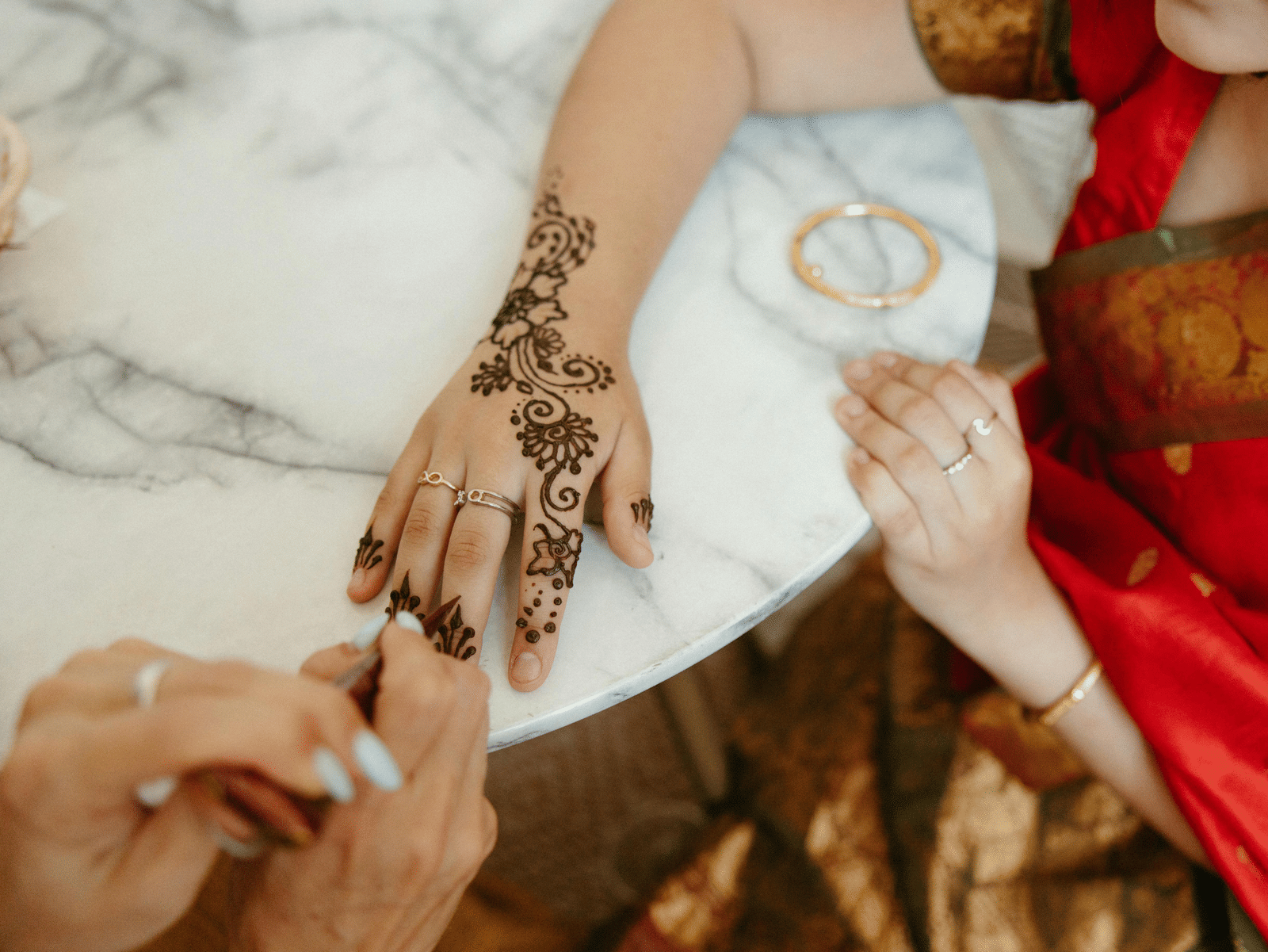 A bride getting intricate mehndi applied on her hand during a pre-wedding ceremony.