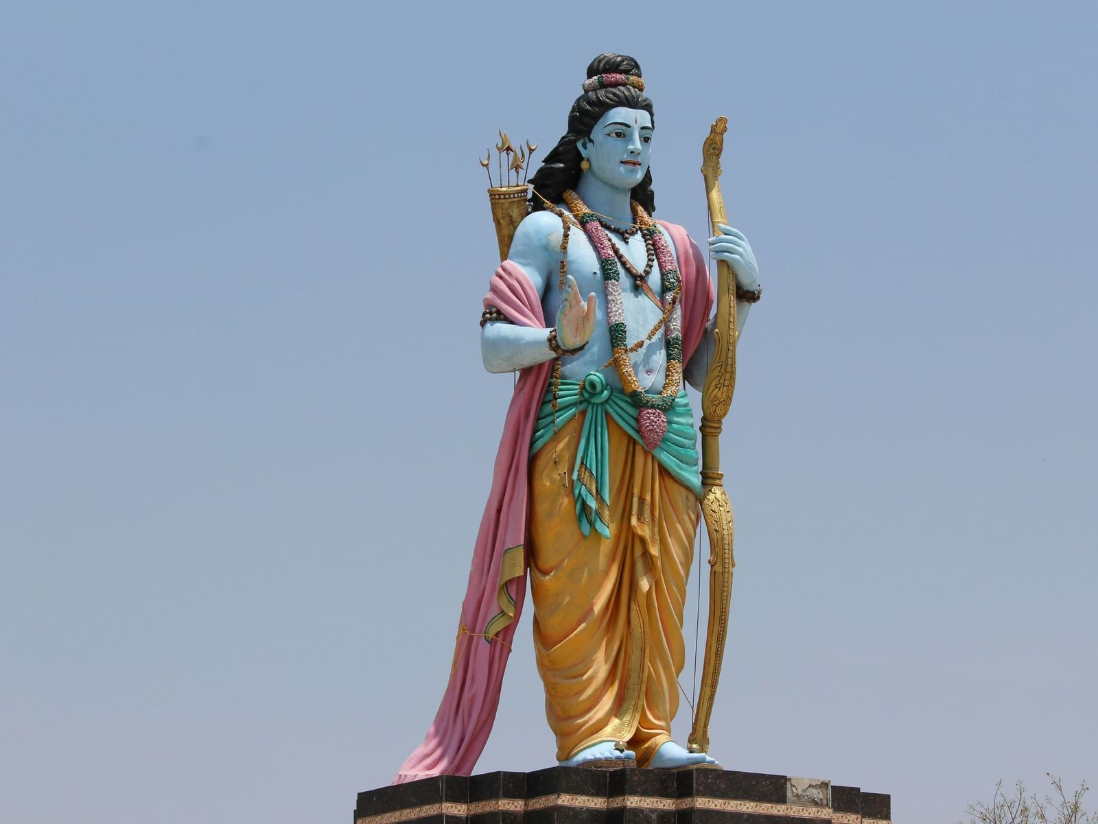Statue of Lord Rama standing with a bow, wearing a dhoti and crown, against a clear sky.