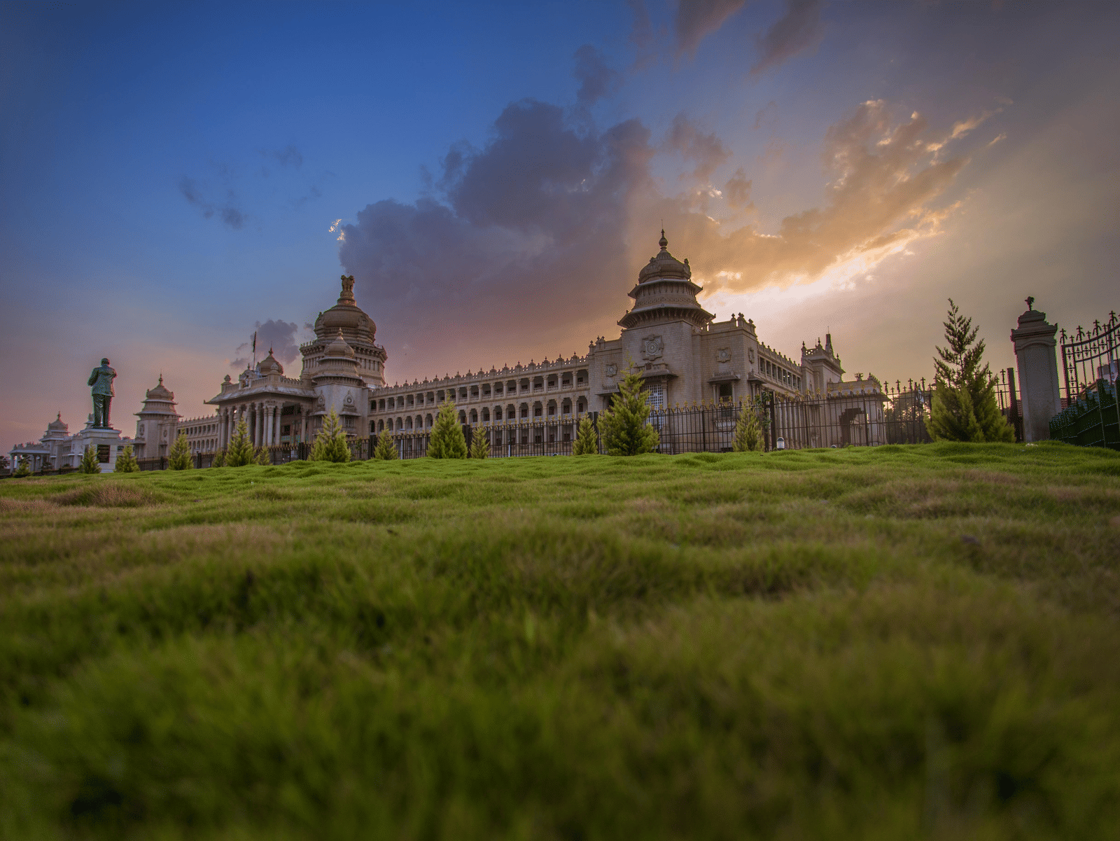 Vidhana soudha building captured at sunset, with dramatic clouds and a lush green foreground creating a serene, majestic landscape.