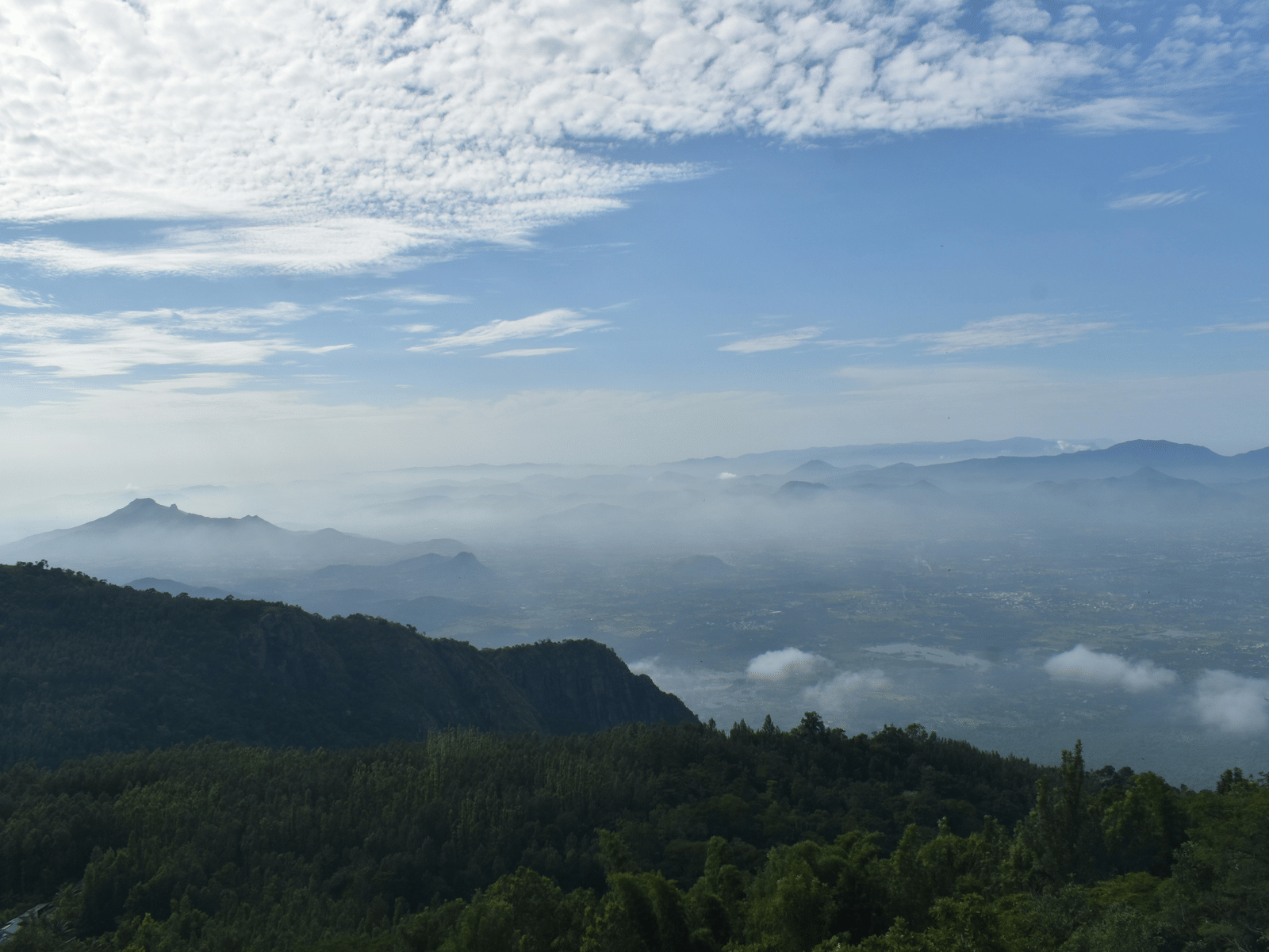A scenic view of rolling hills and valleys blanketed in morning mist under a partly cloudy sky.