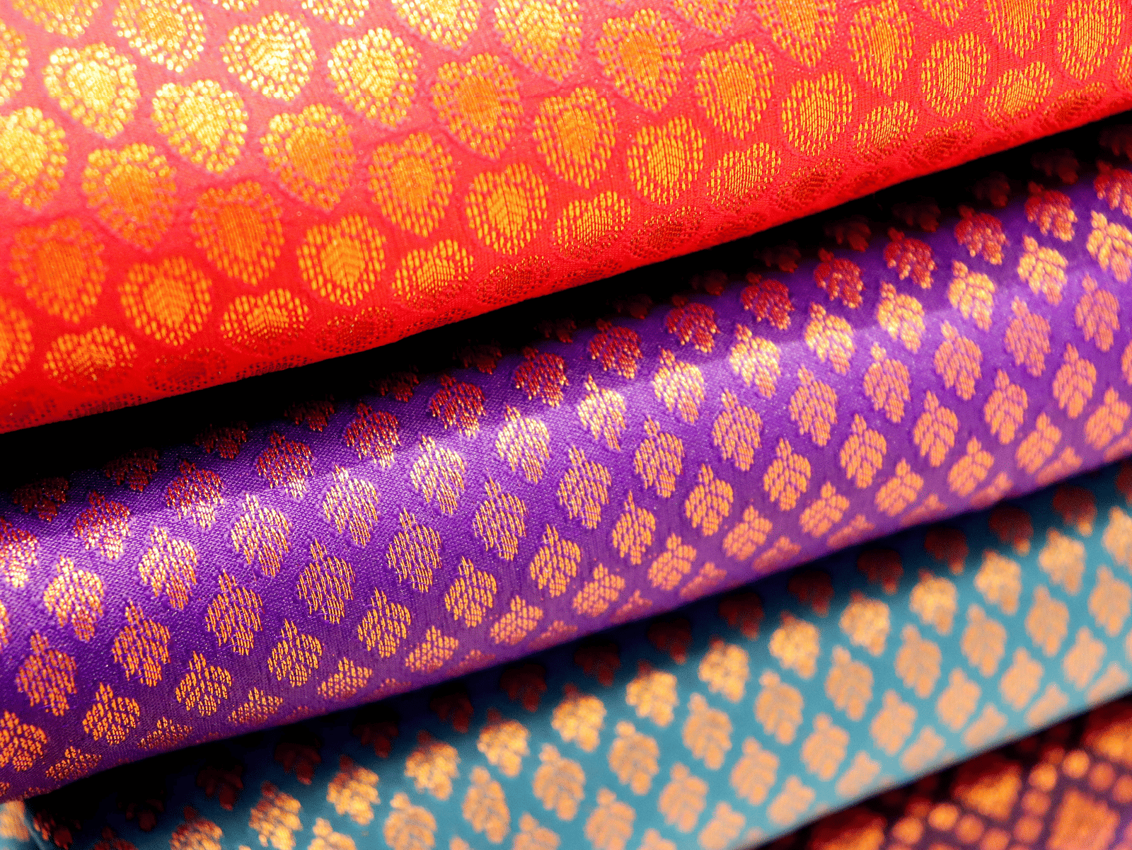A stack of colourful Kanchipuram silk sarees with intricate gold zari patterns.