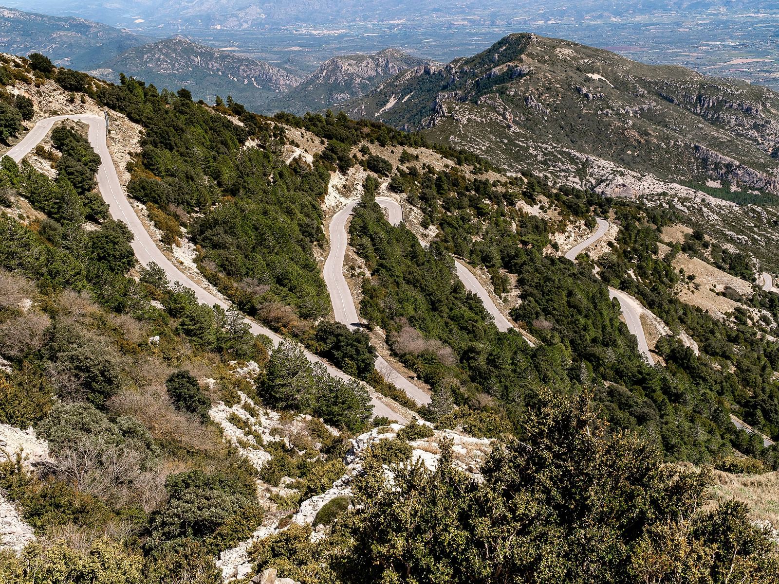 A winding paved road snaking up a mountainside covered in trees and shrubs.