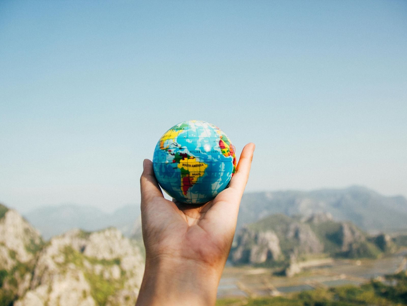 A person's hand holding a mini globe, facing the mountain.
