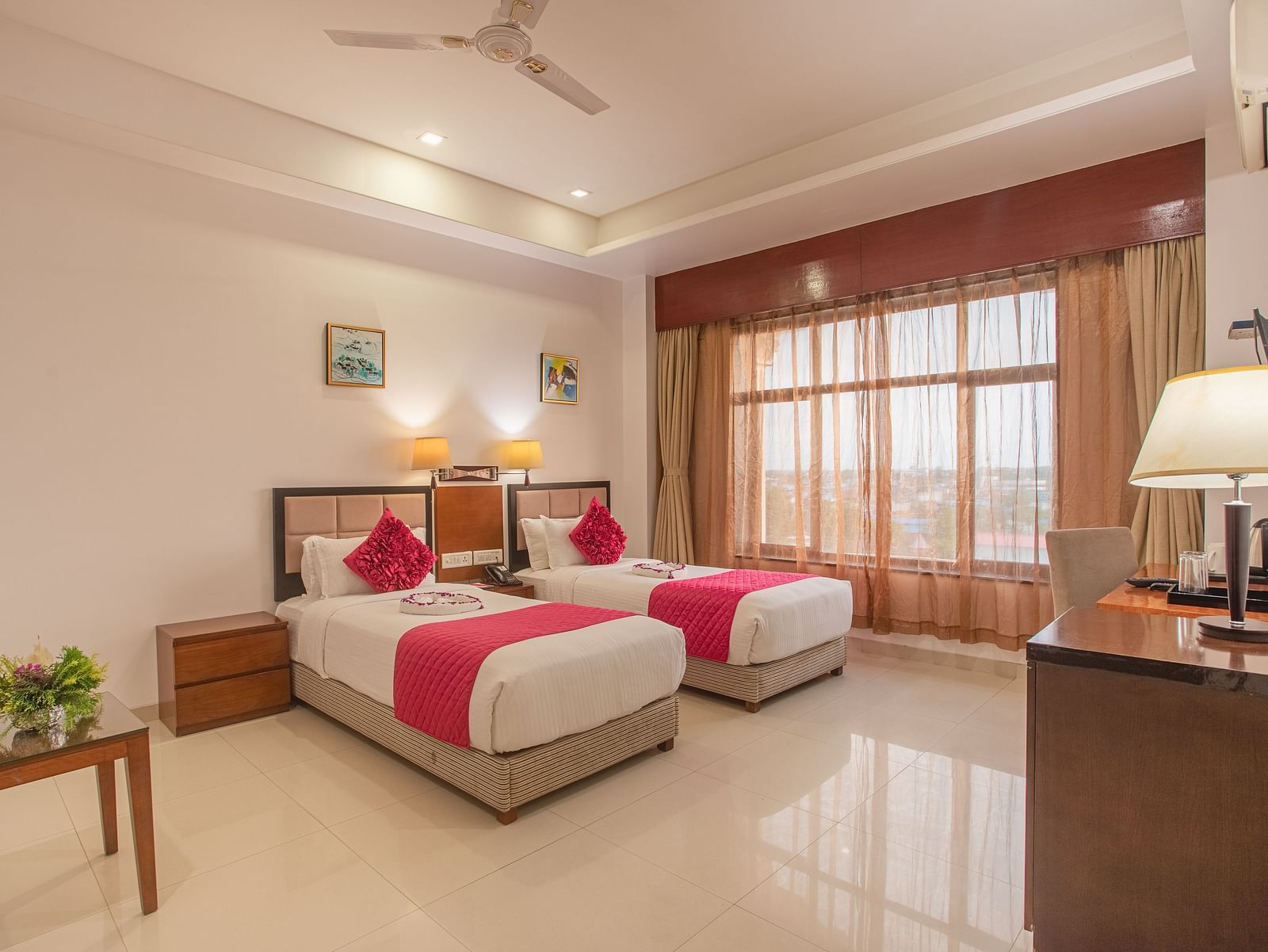 Bright twin room at Diamond Palace Lords Plaza with two single beds featuring pink accents, a work desk, and a small table.