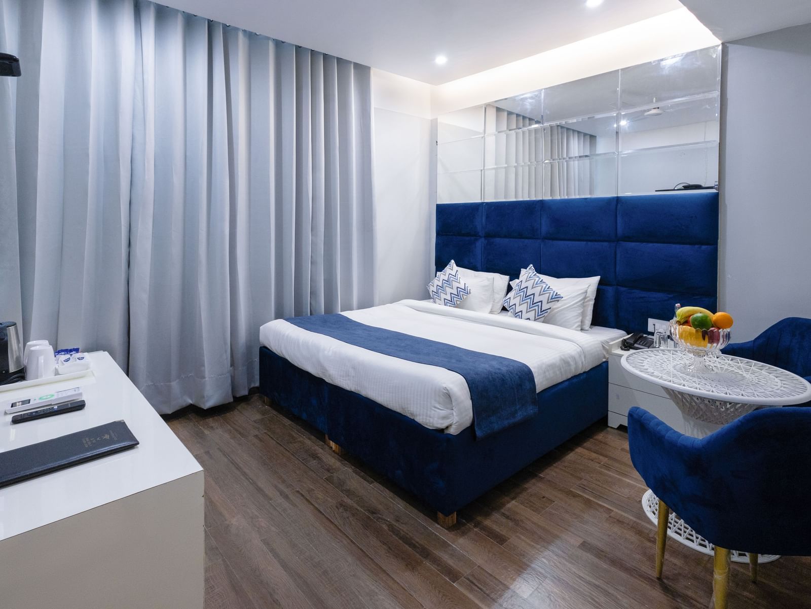 Hotel Room  at Hotel Downtown17, Chandigarh featuring a king size bed with a blue headboard and white and blue linens, two blue chairs with a small round table, and light wood-look flooring. 