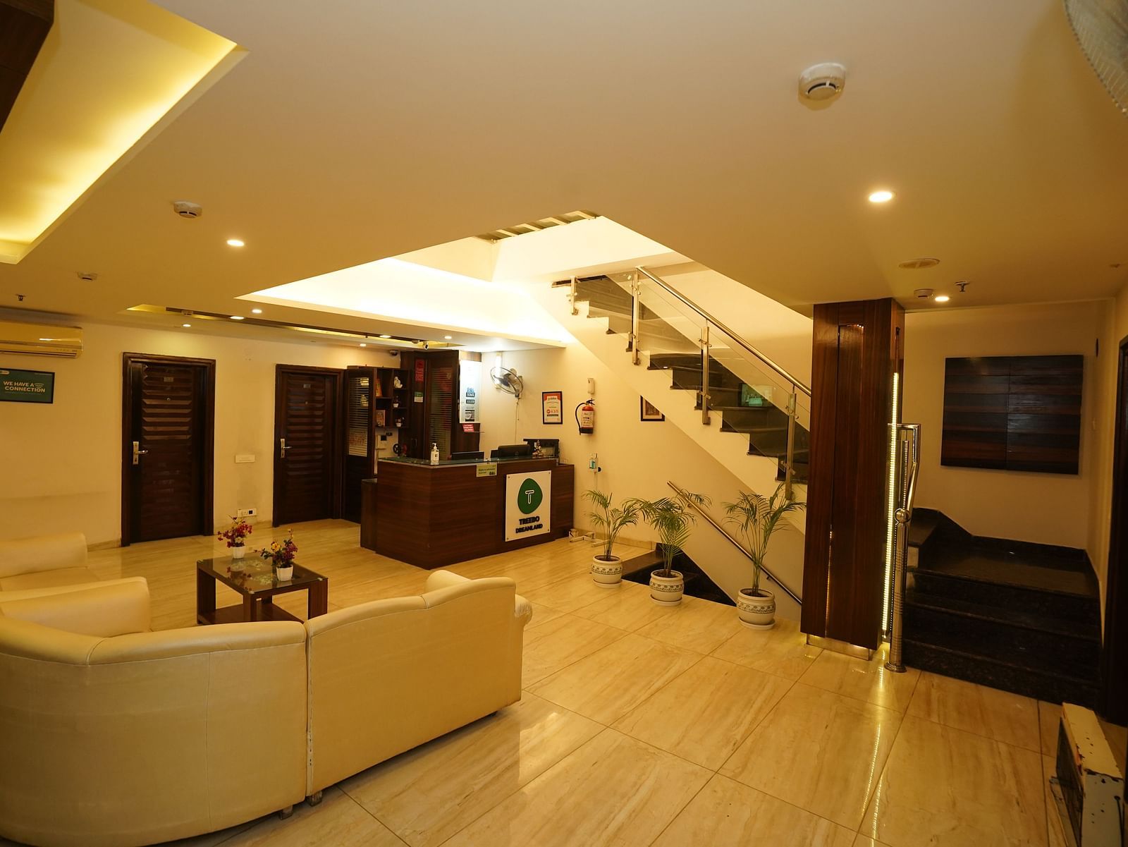 Lobby at Hotel Dreamland, Chandigarh featuring a curved, light-coloured sofa, a dark wood reception desk, and a staircase leading to the upper floors.