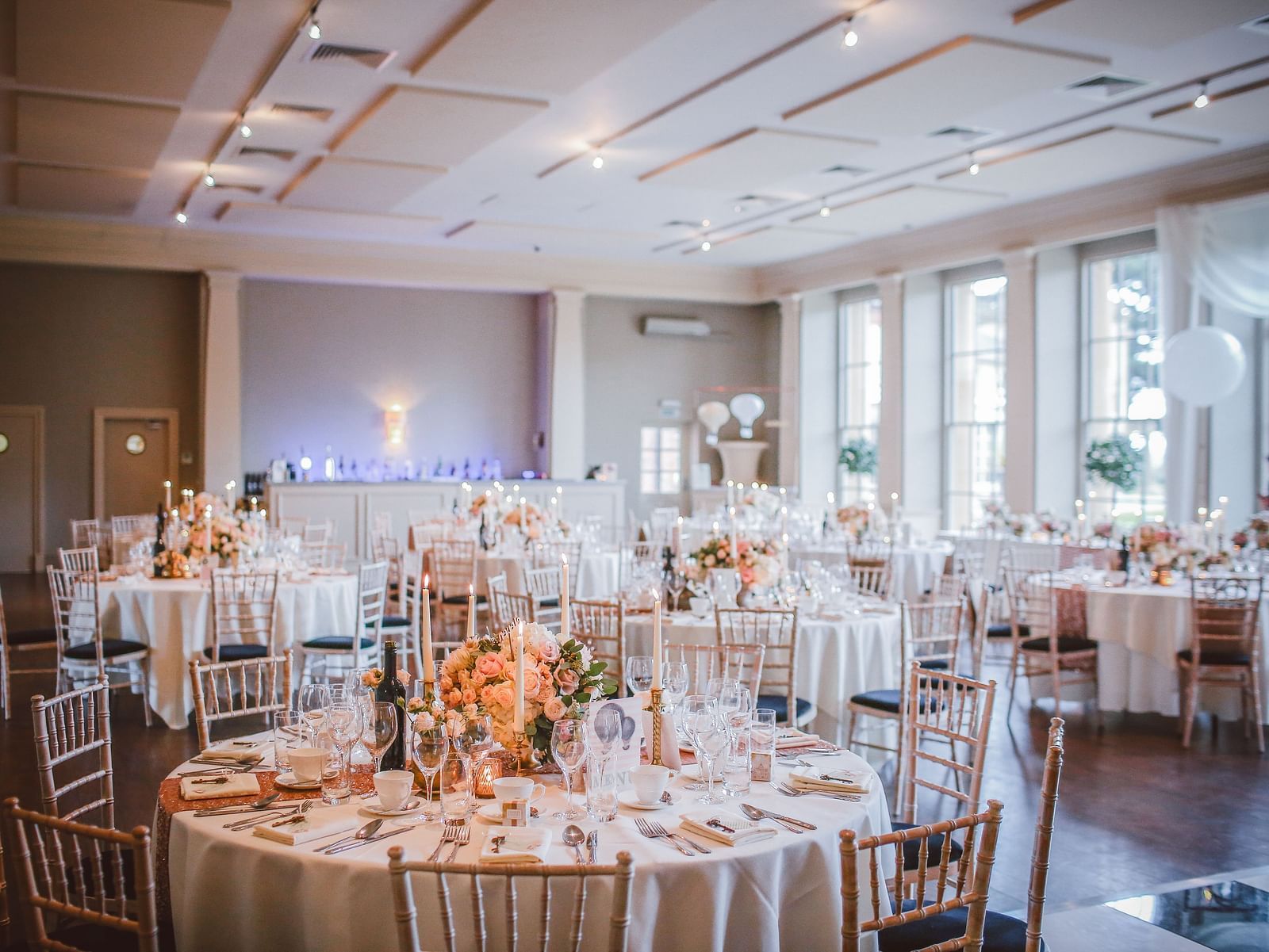 An elaborate banquet hall with round table seating and sun shining through the floor to ceiling windows