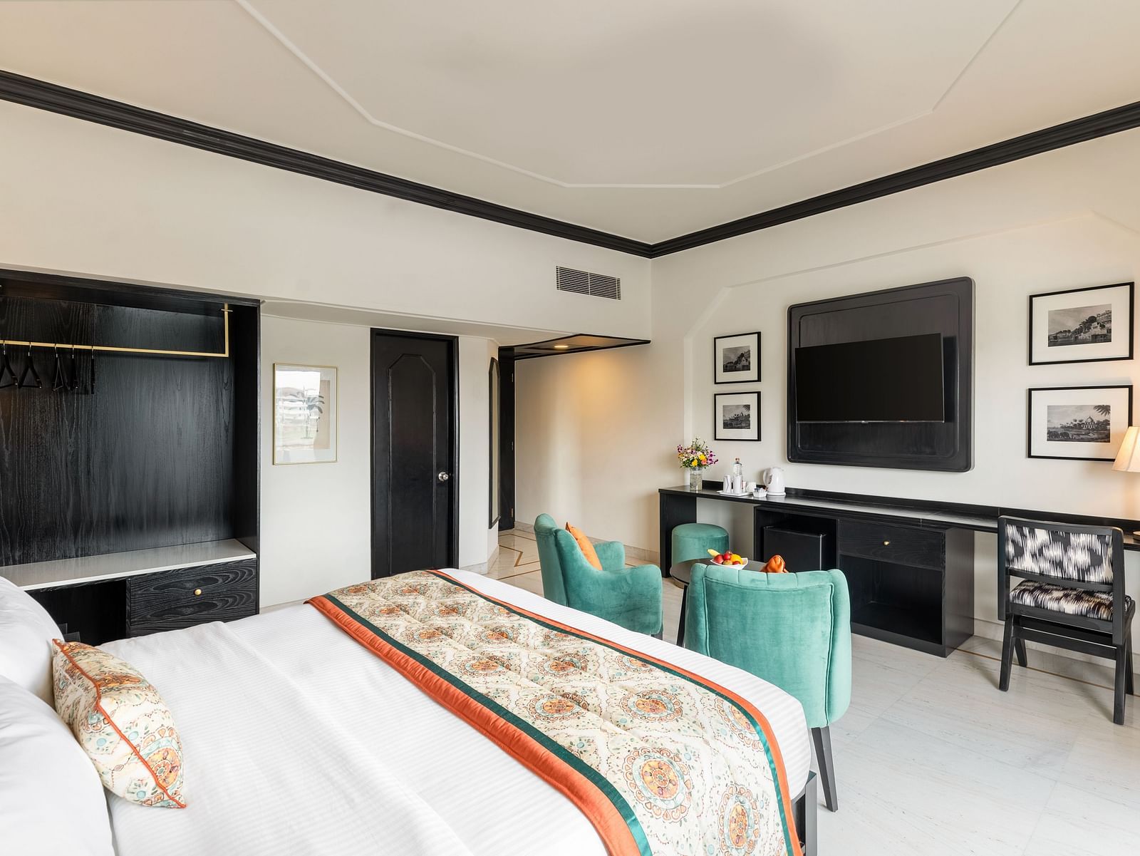 a king size bed in a spacious hotel room in Udaipur featuring two green armchairs, a TV, a wardrobe and several wall paintings - Hotel Rajdarshan, Udaipur.