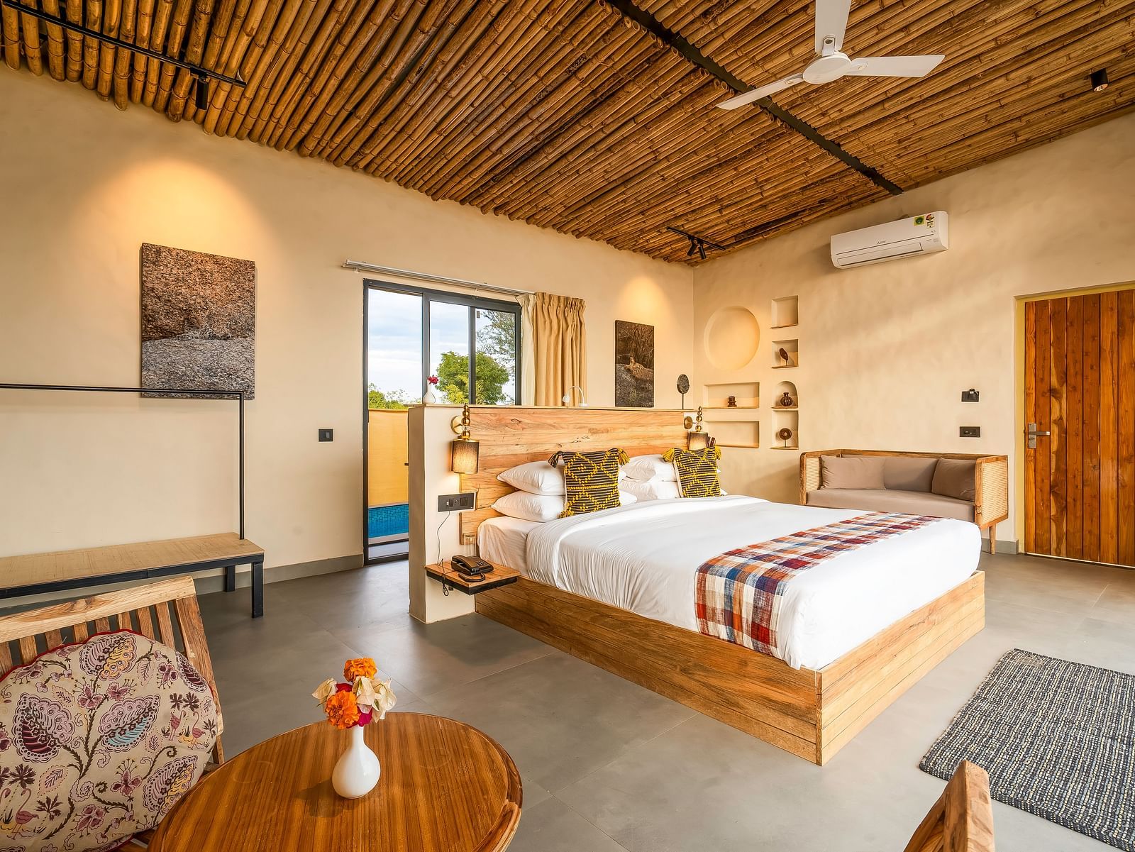 An image of a wooden furnished bedroom  featuring a double size bed, a  chair and centre table, a sofa, AC, fan,  and some decorative items - Kurja Jawai