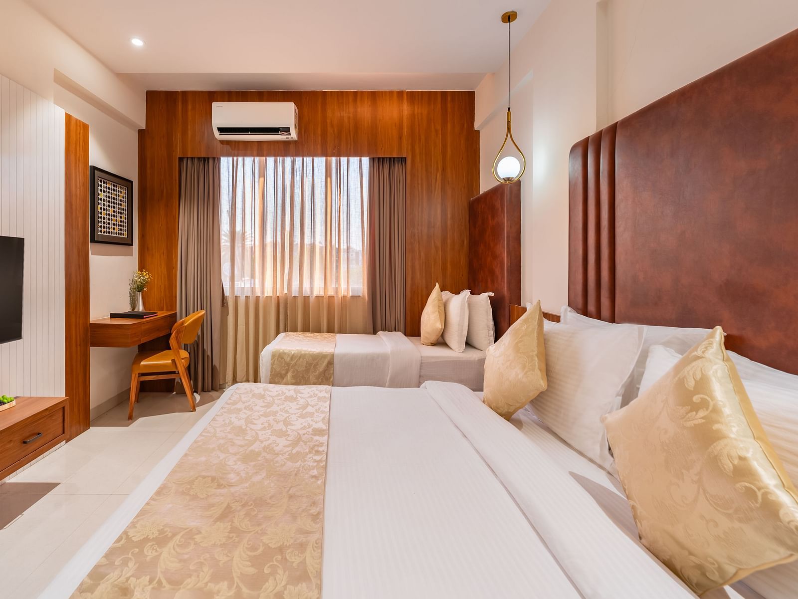 A hotel room offers a large bed and a smaller bed, along with a desk and a mounted television for guests - Lords Eco Inn Ambaji.