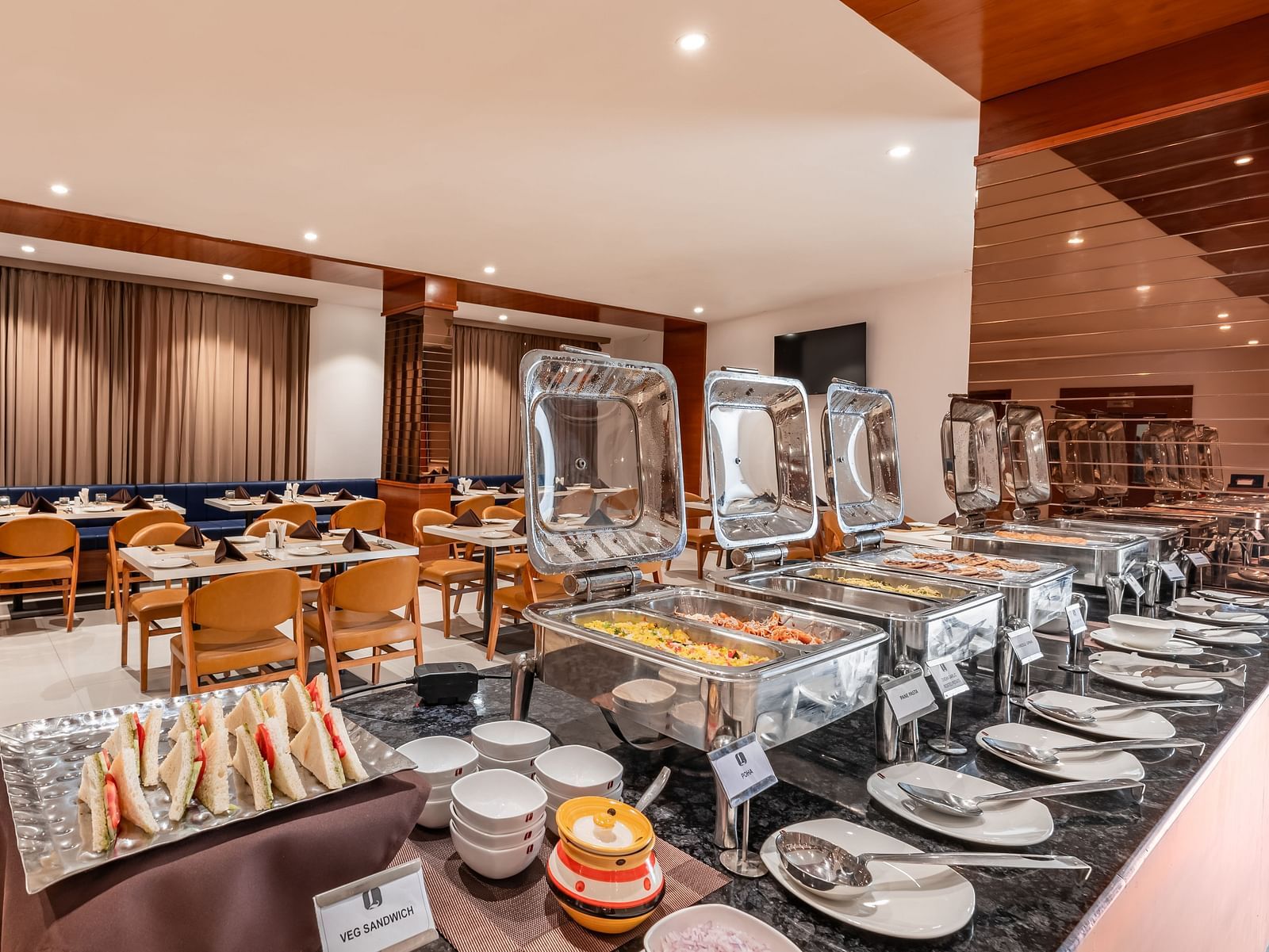 A buffet spread with covered food warmers, plates, and other serving dishes is ready in a dining area - Lords Eco Inn Ambaji.