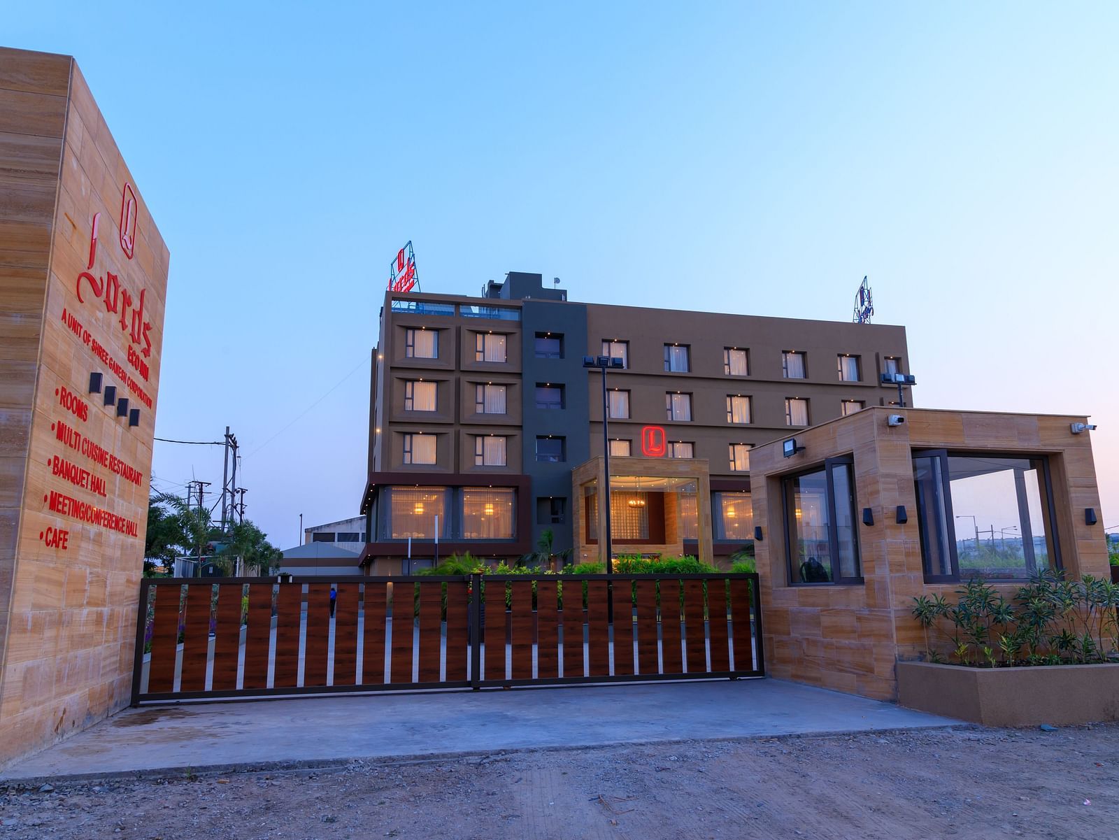 The exterior of Lords Eco Inn Apple Gate is viewed from the entrance, showing the multi-storey building, signage, and surrounding gates under a clear sky.