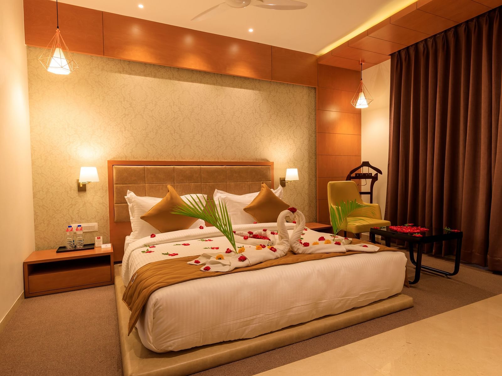 A warmly lit hotel room at Lords Eco Inn Apple Gate features a decorated double bed, bedside tables, a chair, and brown curtains.