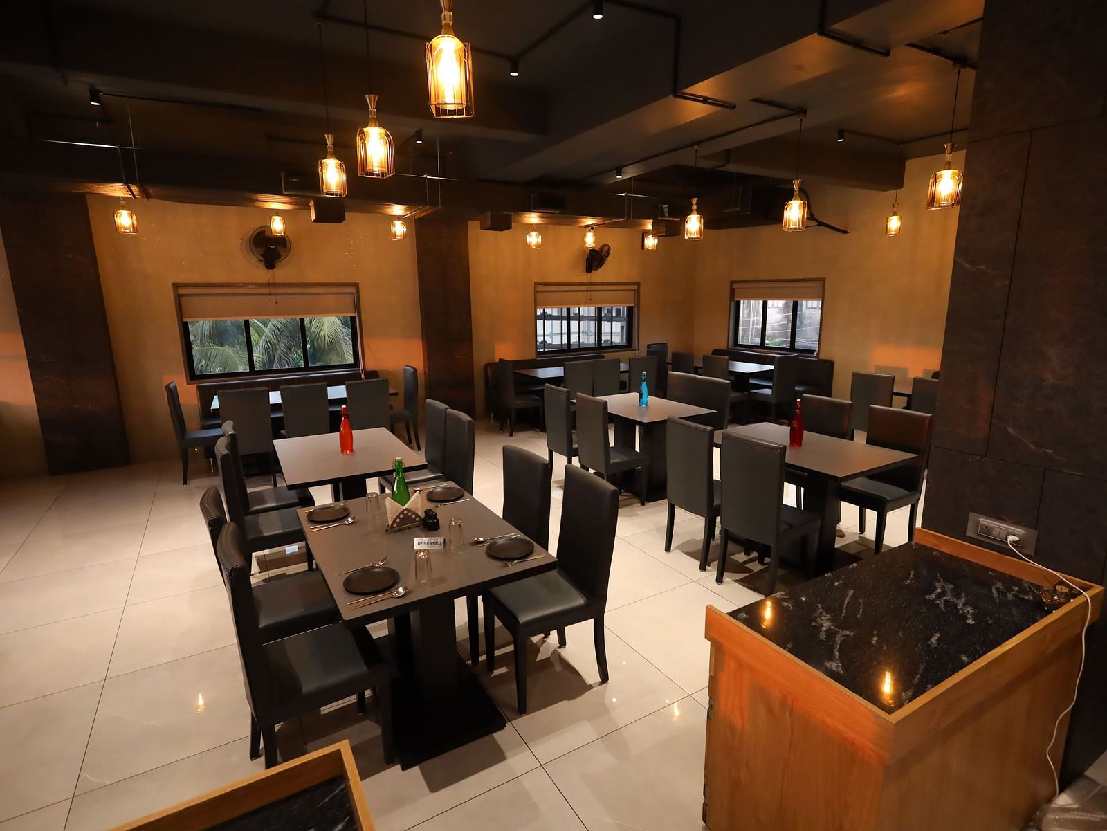 The image depicts a restaurant interior with set tables and chairs under warm, hanging lights - Lords Eco Inn Navsari.