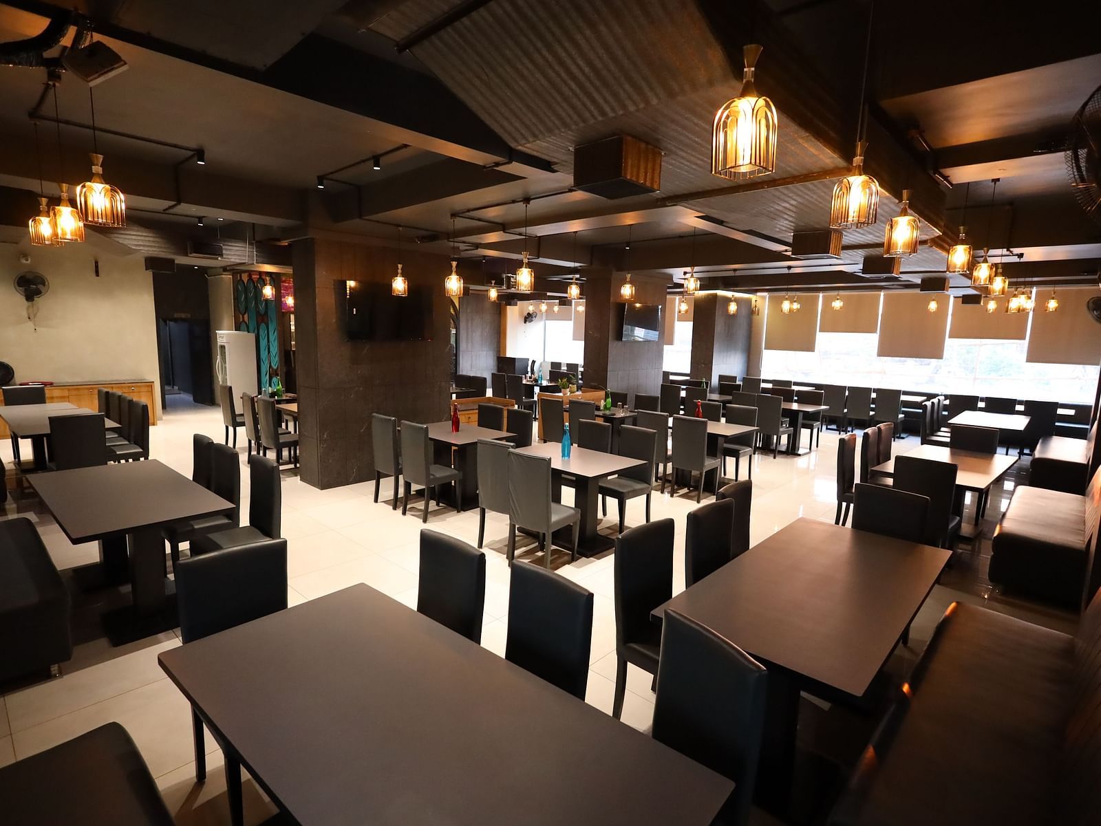The image shows the interior of a restaurant with multiple tables and chairs under warm lighting - Lords Eco Inn Navsari.
