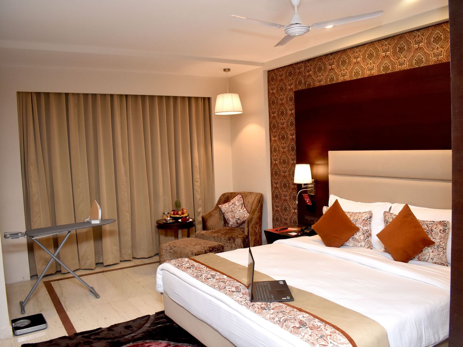A hotel room features a bed with a laptop and bedside lighting at Lords Plaza Surat.