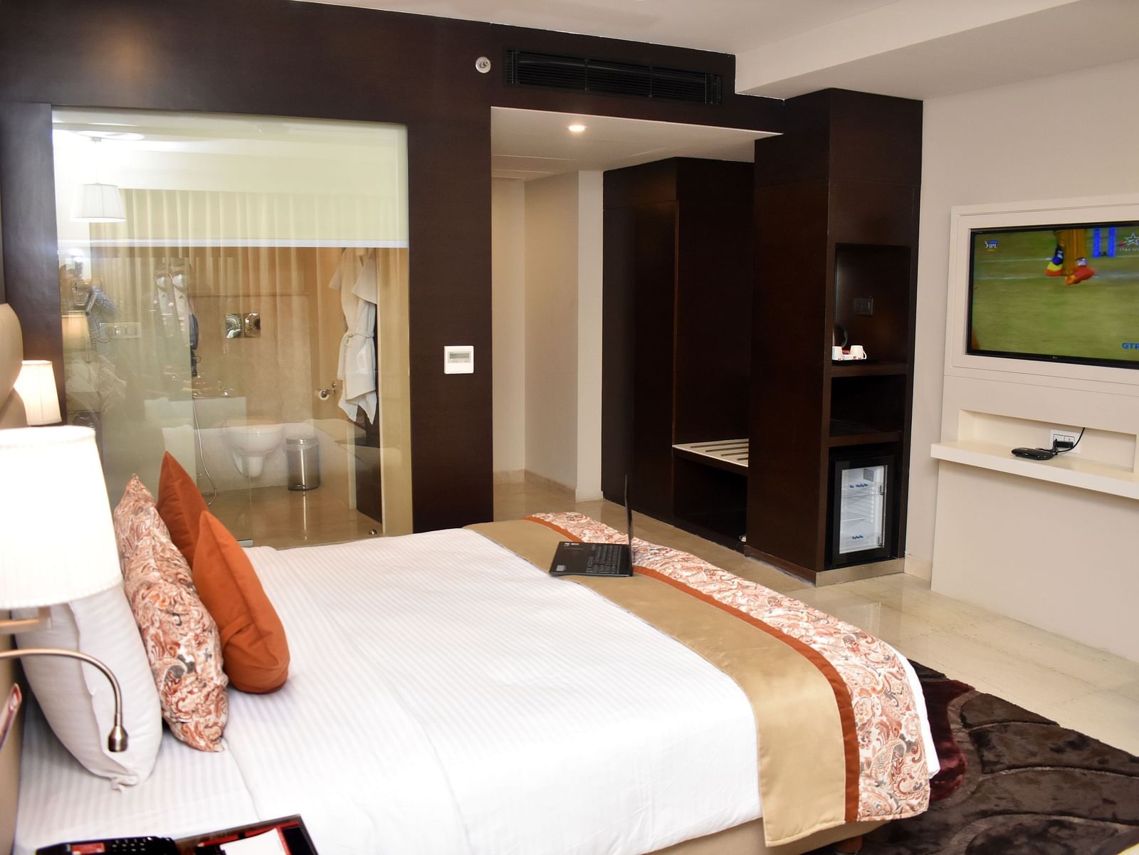 A hotel room features a bed, television, and open closet space at Lords Plaza Surat.