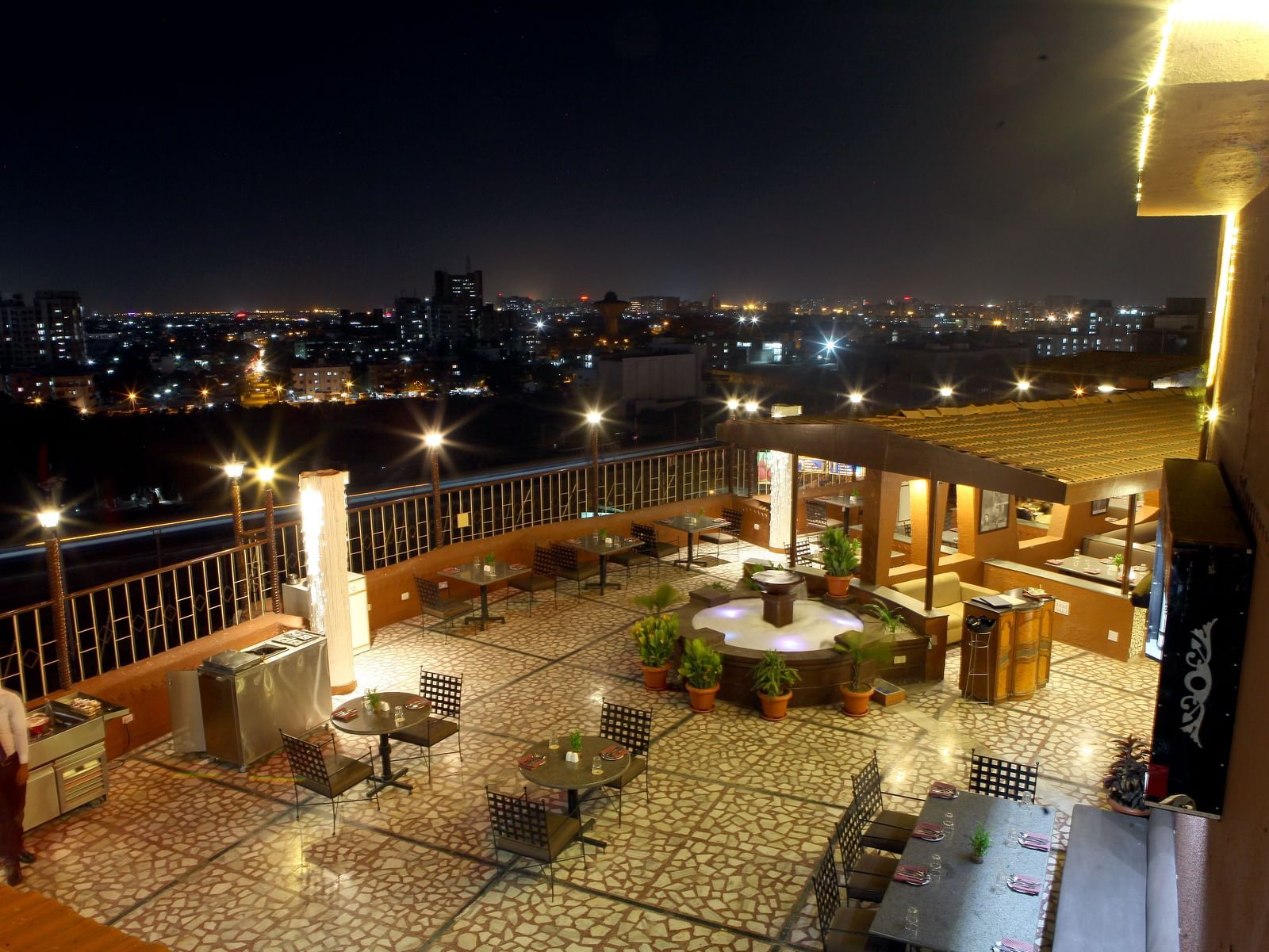An outdoor seating area with city lights visible at night at Lords Plaza Surat.