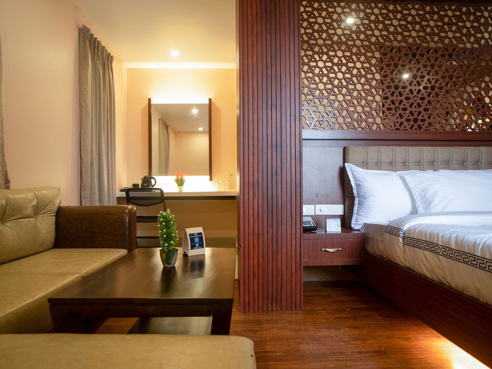 A hotel room interior featuring a sofa, coffee table, bed, and decorative wall panel | Mansha Hotels