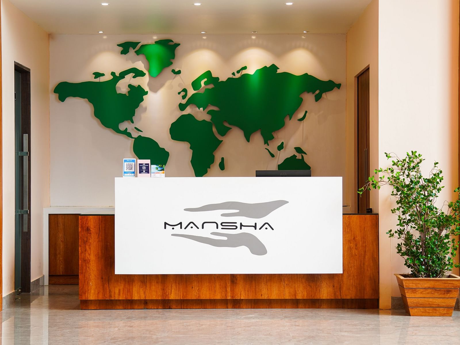 A hotel reception area with a world map on the wall and the 'Mansha' logo on the counter | Mansha Hotels