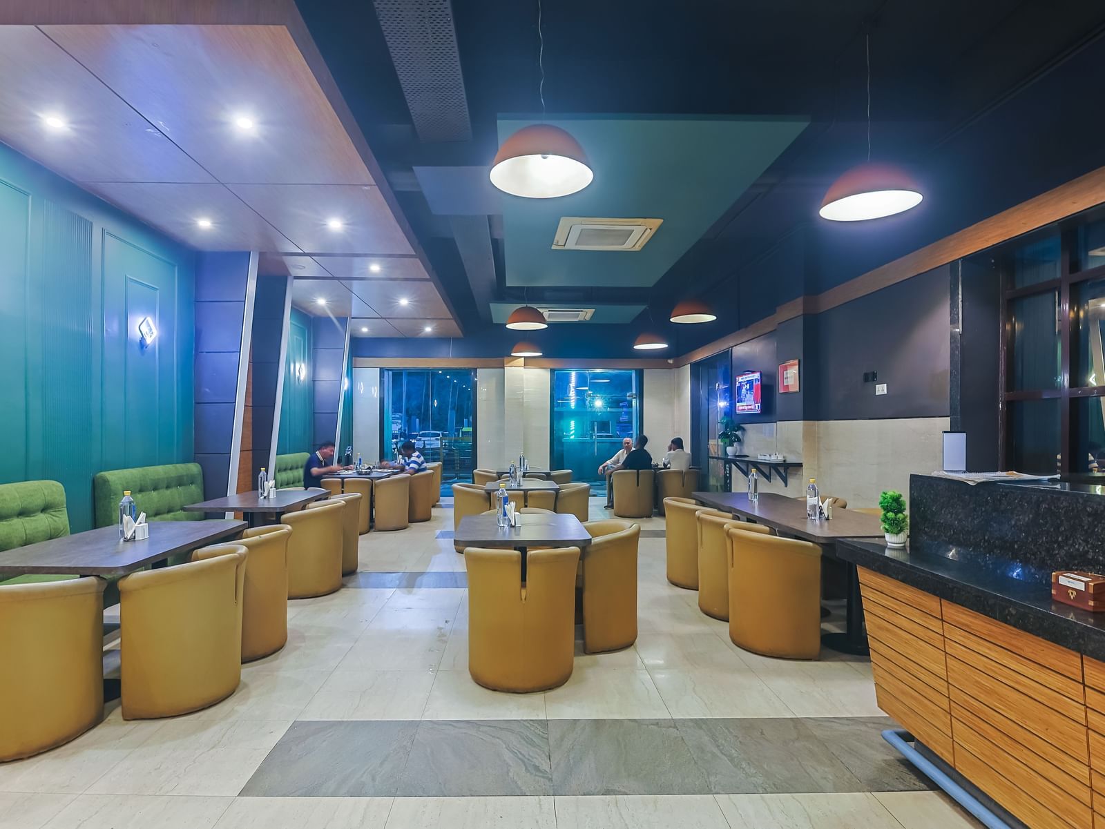 Restaurant with multiple dining tables, green accents and ceiling lights at Max Hotel Prayagraj.