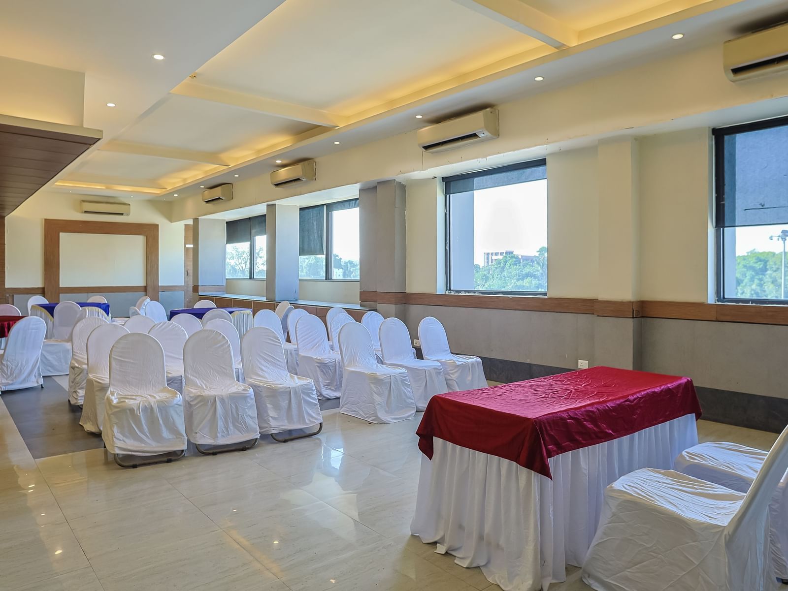 Banquet hall with rectangular tables, white chairs and large windows at Max Hotel Prayagraj.