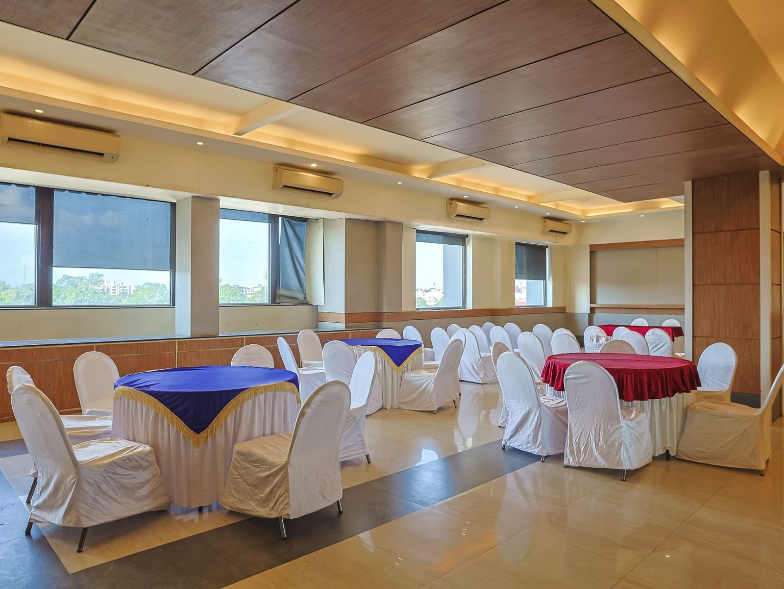 Banquet hall with white chairs, wooden ceiling and bright lighting at Max Hotel Prayagraj.