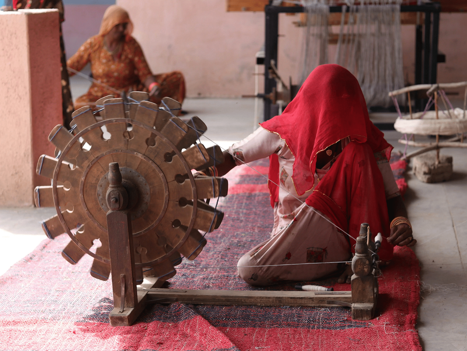 Two individuals, one operating a traditional spinning wheel (charkha), likely making Khadi fabric.